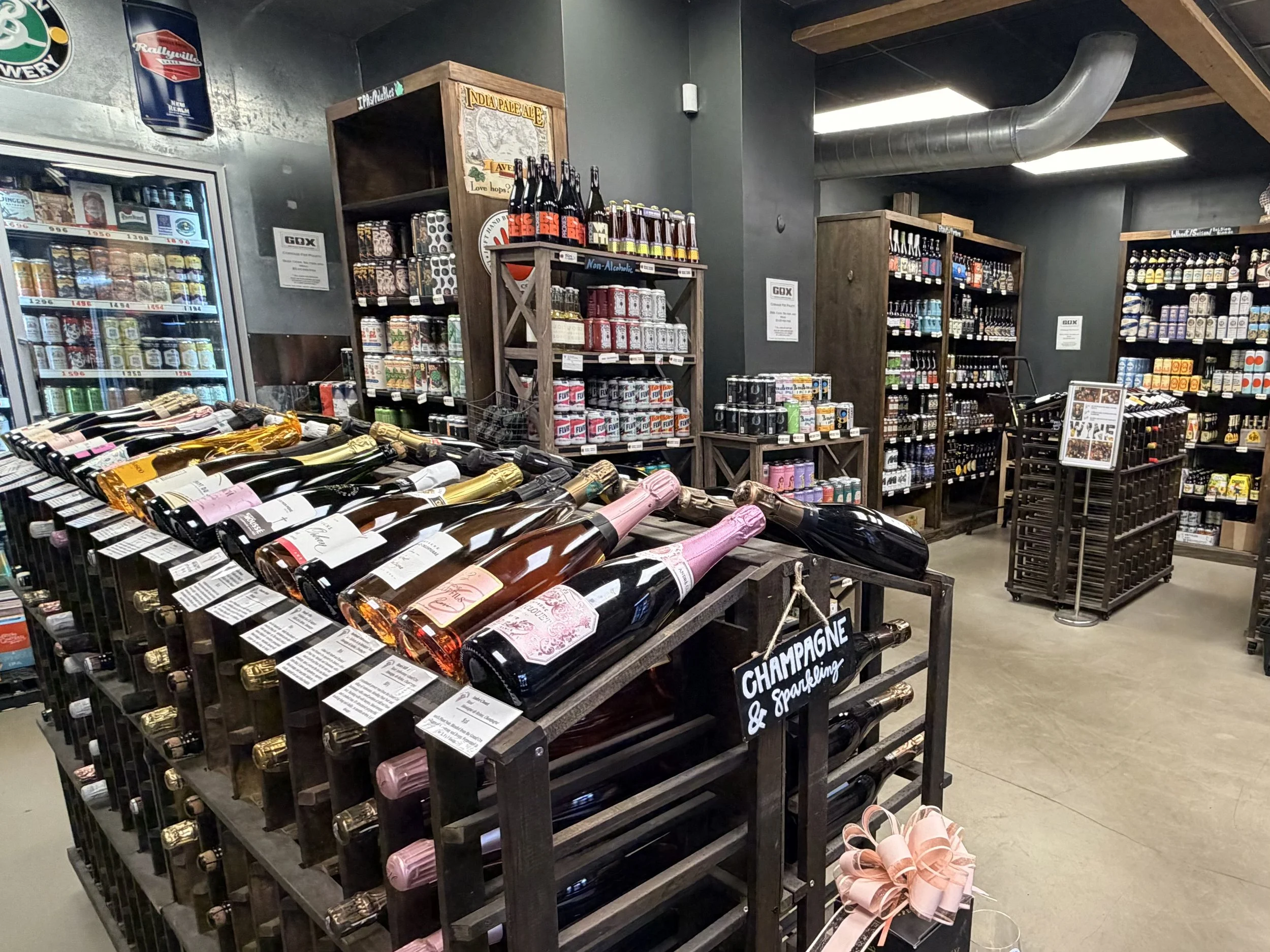 A wide-angle interior shot of the Greenville Beer Exchange retail space. The image features impressive floor-to-ceiling shelving stocked with a vast craft beer selection, alongside  rolling wine shelves.