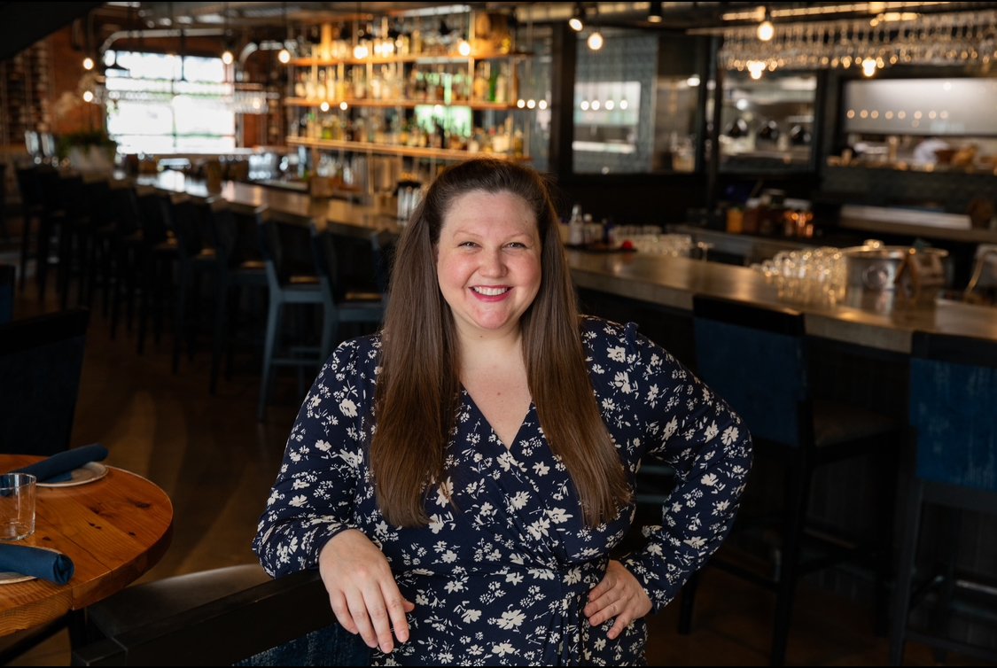 A professional headshot of Sommelier Amy smiling warmly in an elegant restaurant setting.