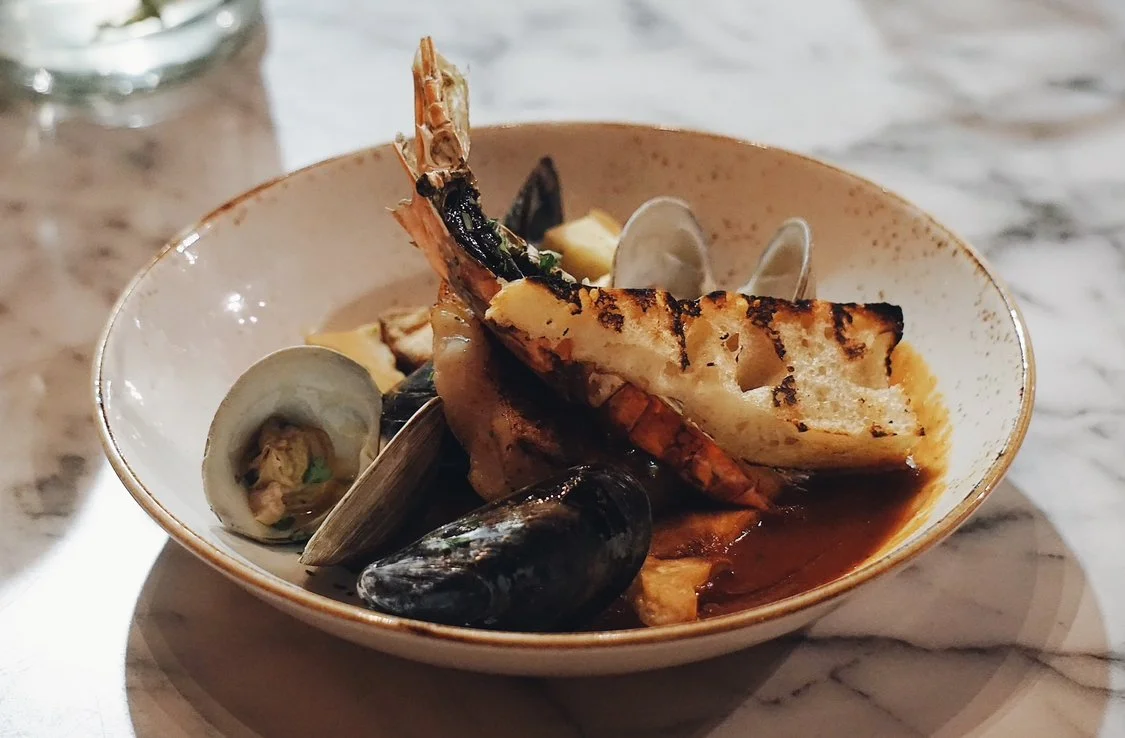 An elegantly plated Clams Provençal dish featuring fresh shellfish in a vibrant herb broth, served with thick slices of toasted crusty bread. A masterfully prepared seafood course showcasing artisan culinary technique.