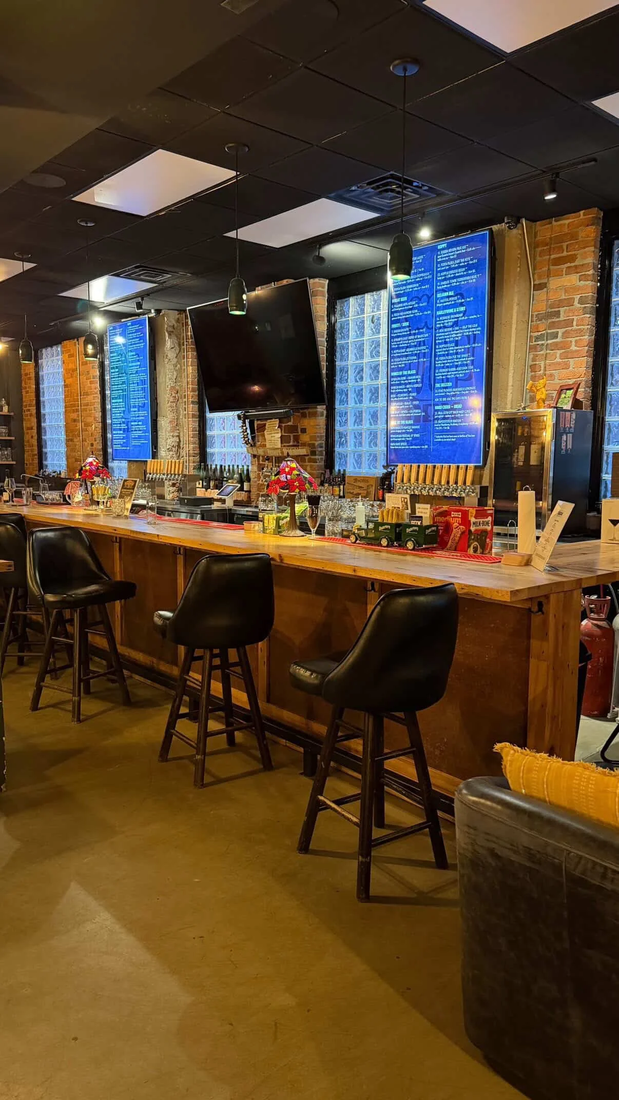 A shot of the bar at Greenville Beer Exchange. Two large digital screens display the current beer and wine selections above, while the bar is styled with red stained-glass lamps and large black stools