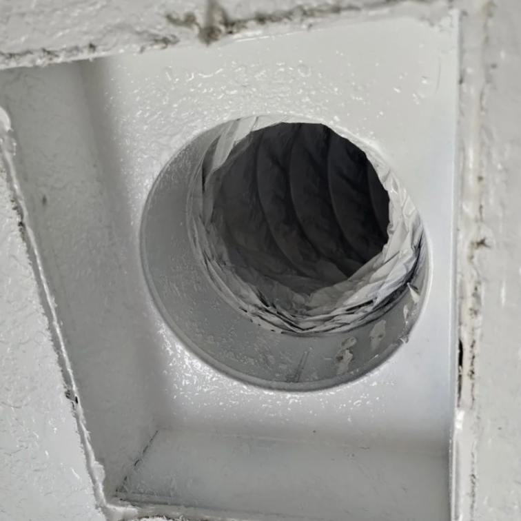 A close-up view of a vent with a white frame, with the interior lined with crumpled foil or metallic material, mounted on a white painted surface.