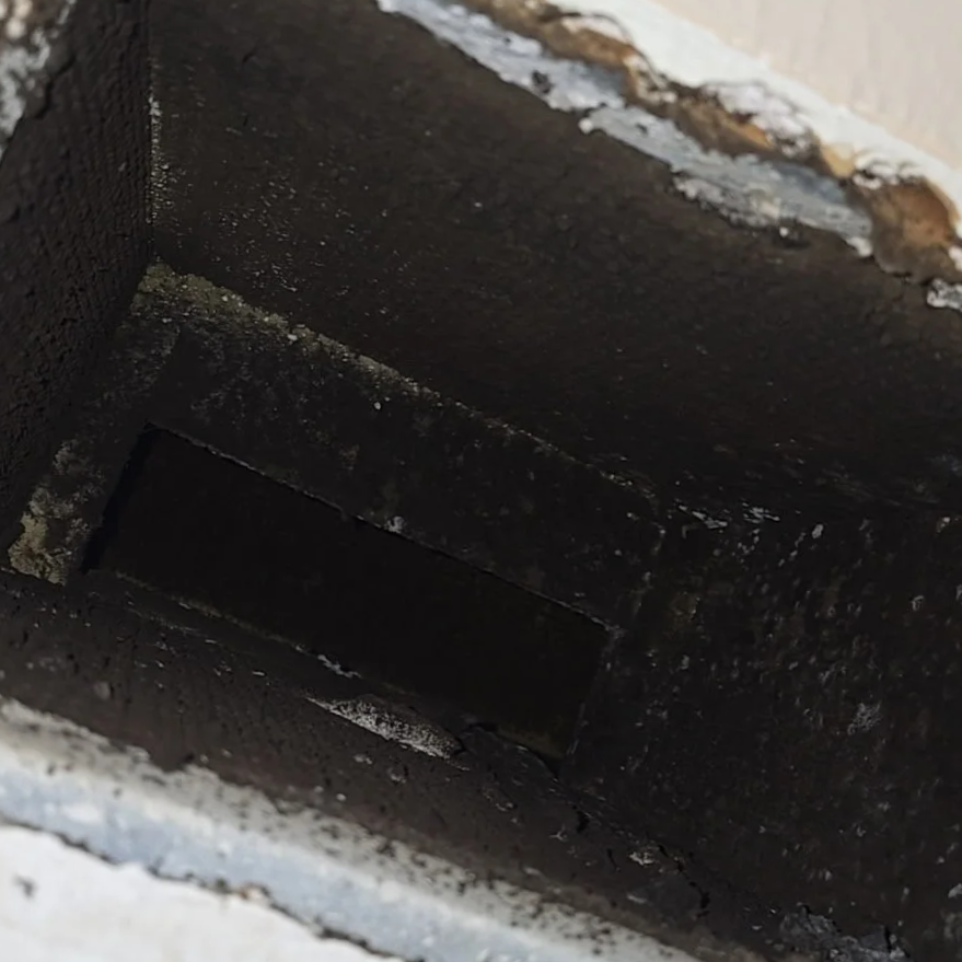 Close-up of a black, rectangular, hollow vent or duct with some debris and rust around its edges.