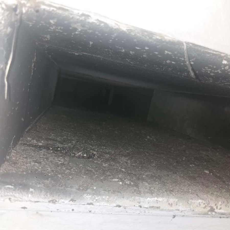 Close-up of a dusty, black, rectangular vent or duct with some dust and dirt buildup.
