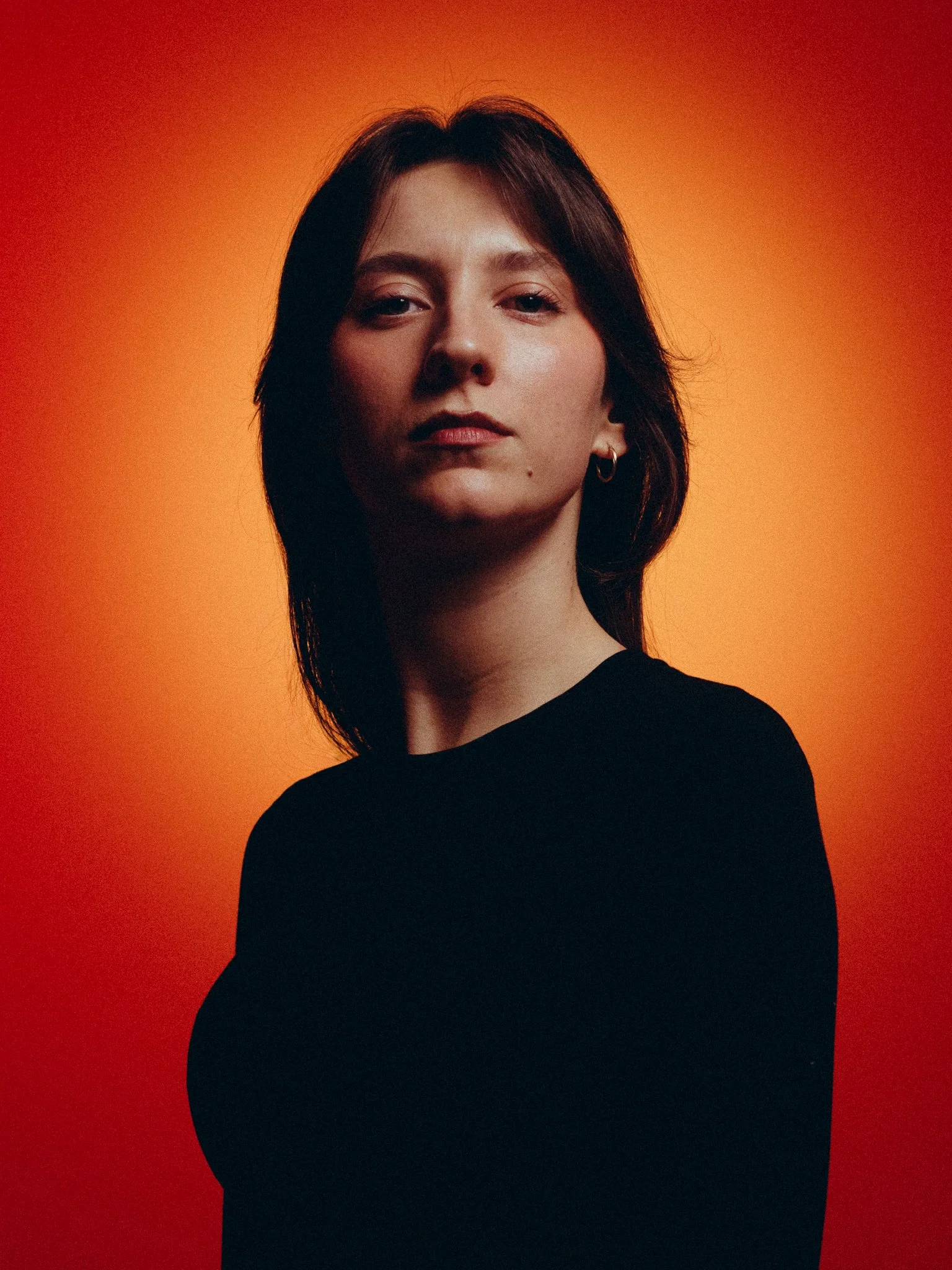 Portrait of a woman with dark hair wearing a black top against an orange gradient background.