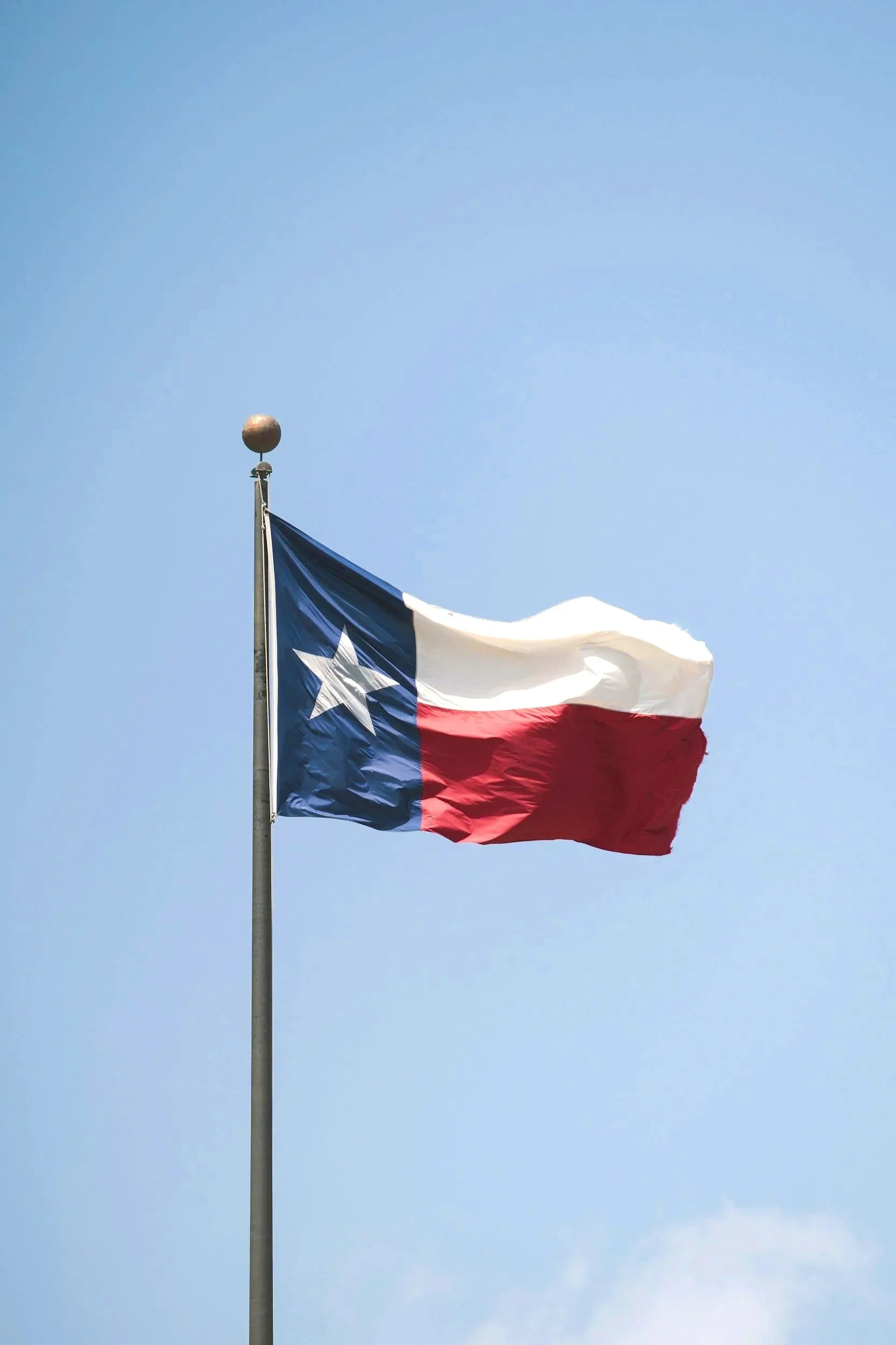 The Texas state flag waving against blue sky.