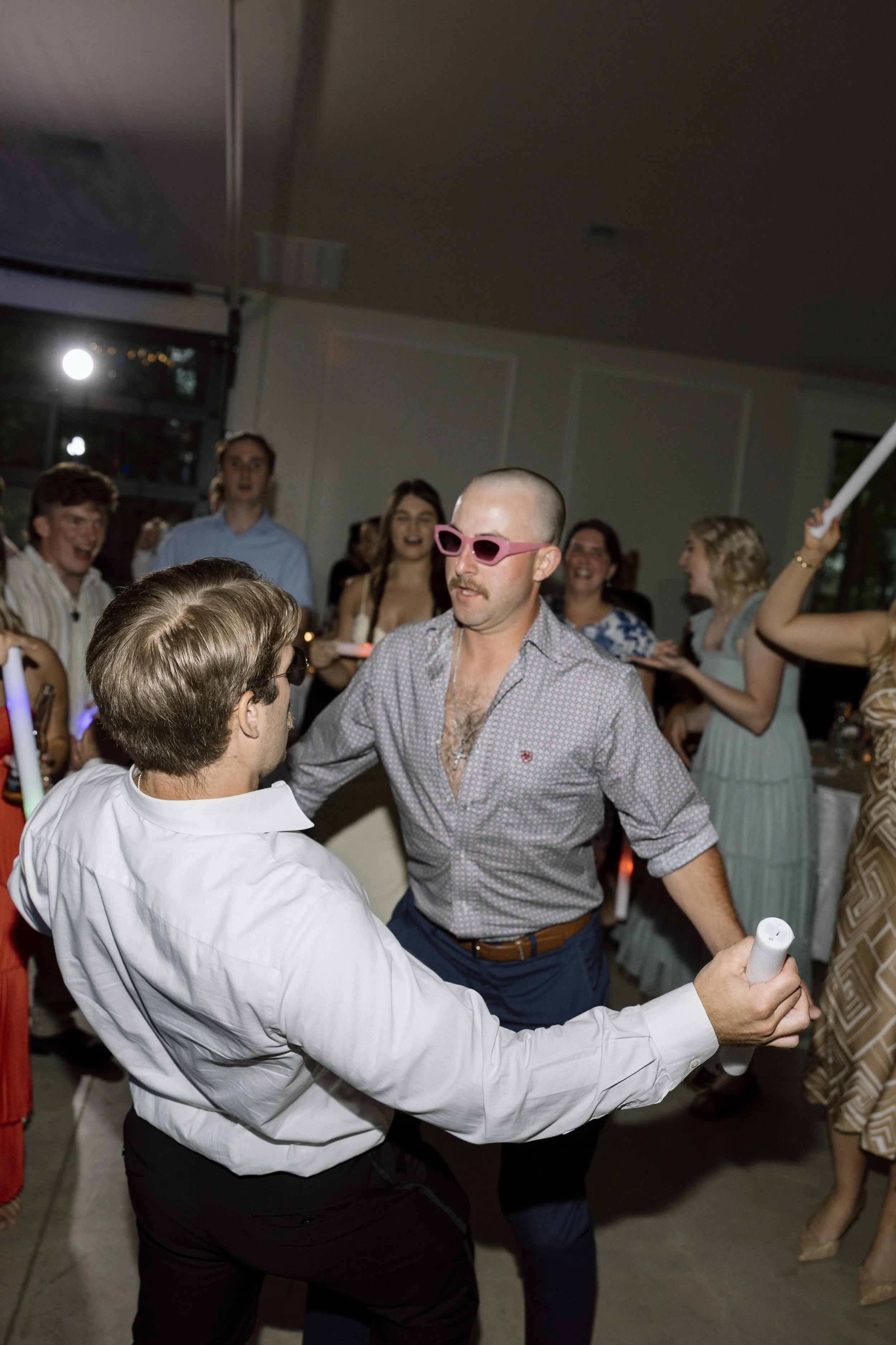 People dancing and celebrating at a party, some wearing glasses and holding glow sticks.