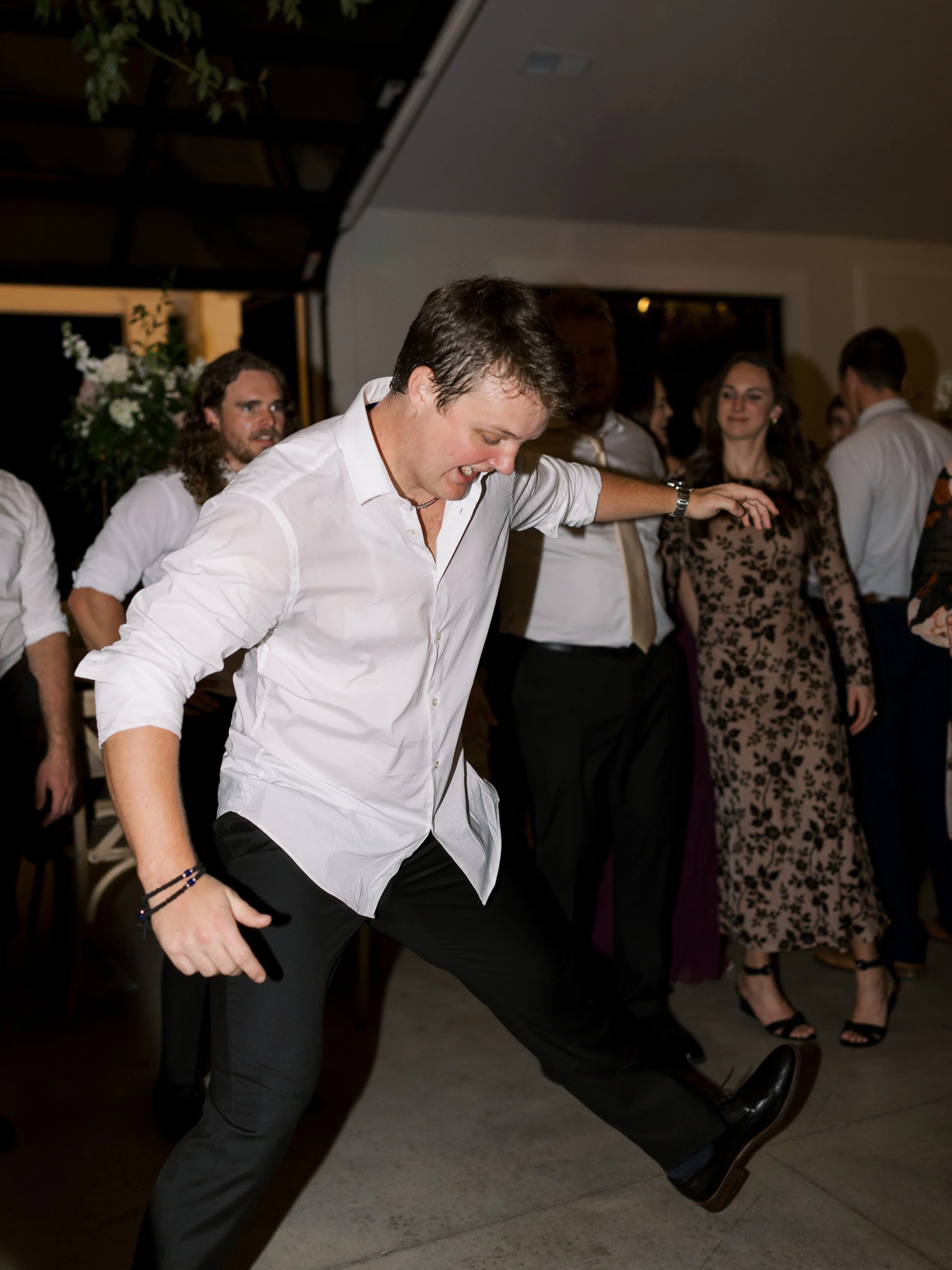 Person dancing at an indoor party with other guests in the background.