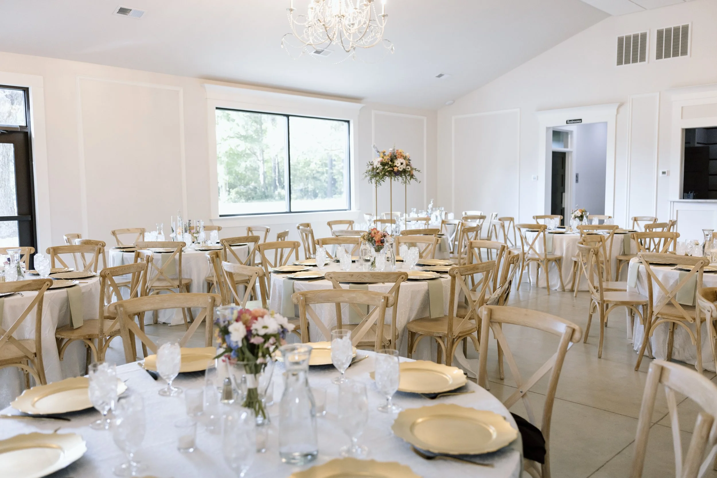 An elegant banquet hall decorated with white tablecloths and floral centerpieces, set for a formal event.