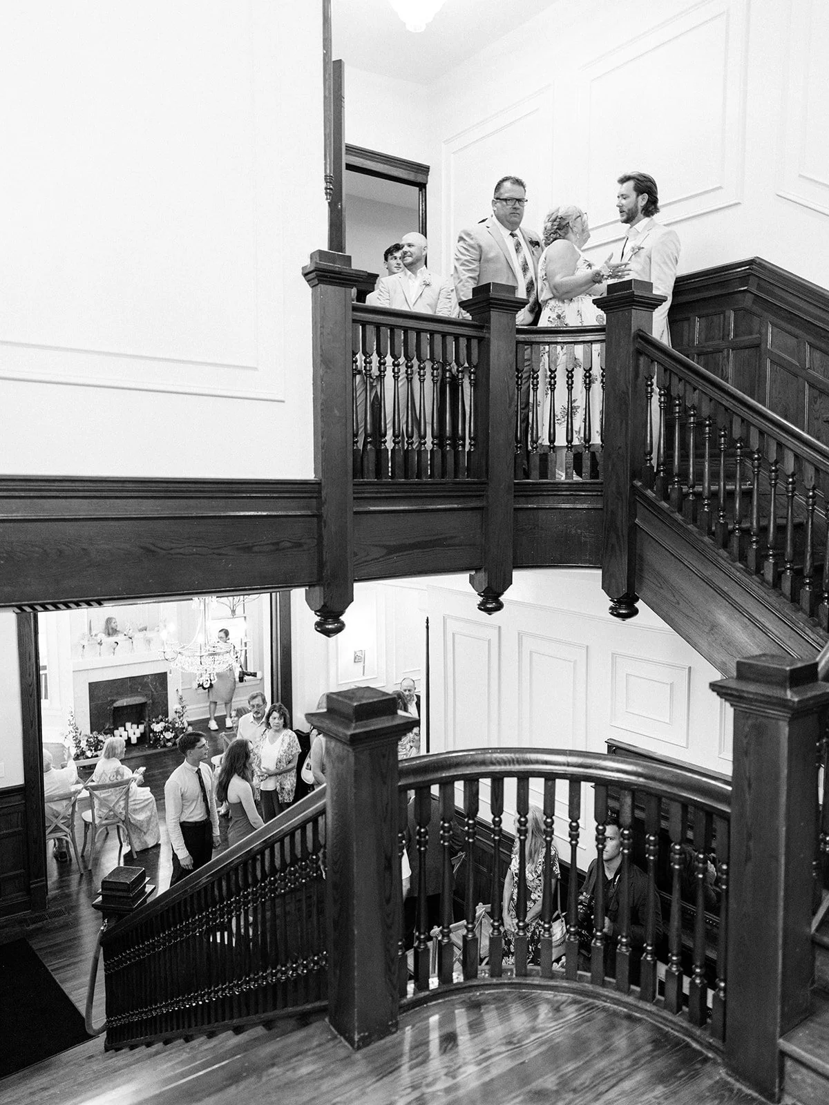 People gathered on a staircase and in a living room in a home, attending a social event or gathering, in black and white.