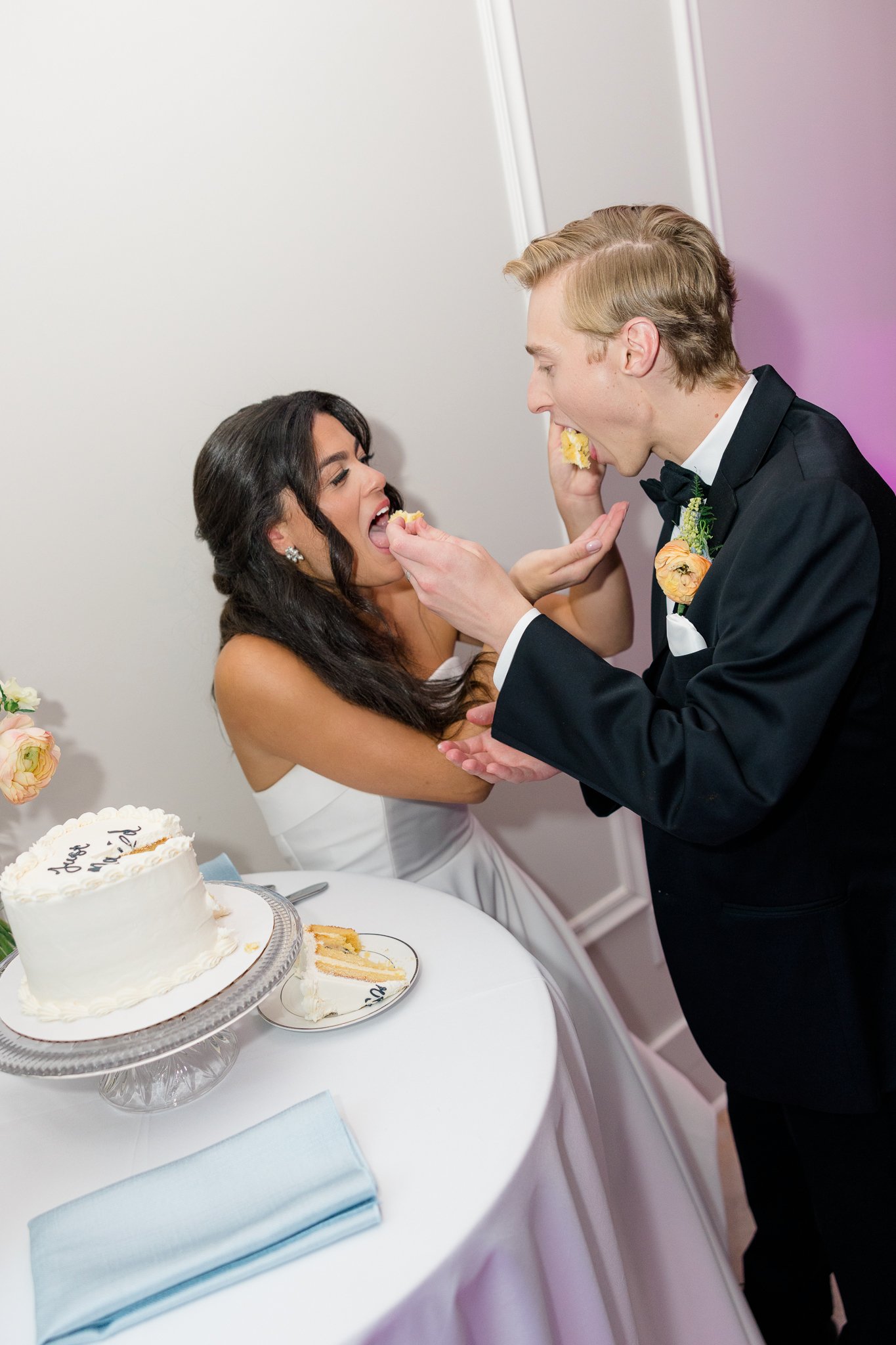 A newlywed couple sharing a cake at their wedding reception, with a white frosted cake on a table in front of them.