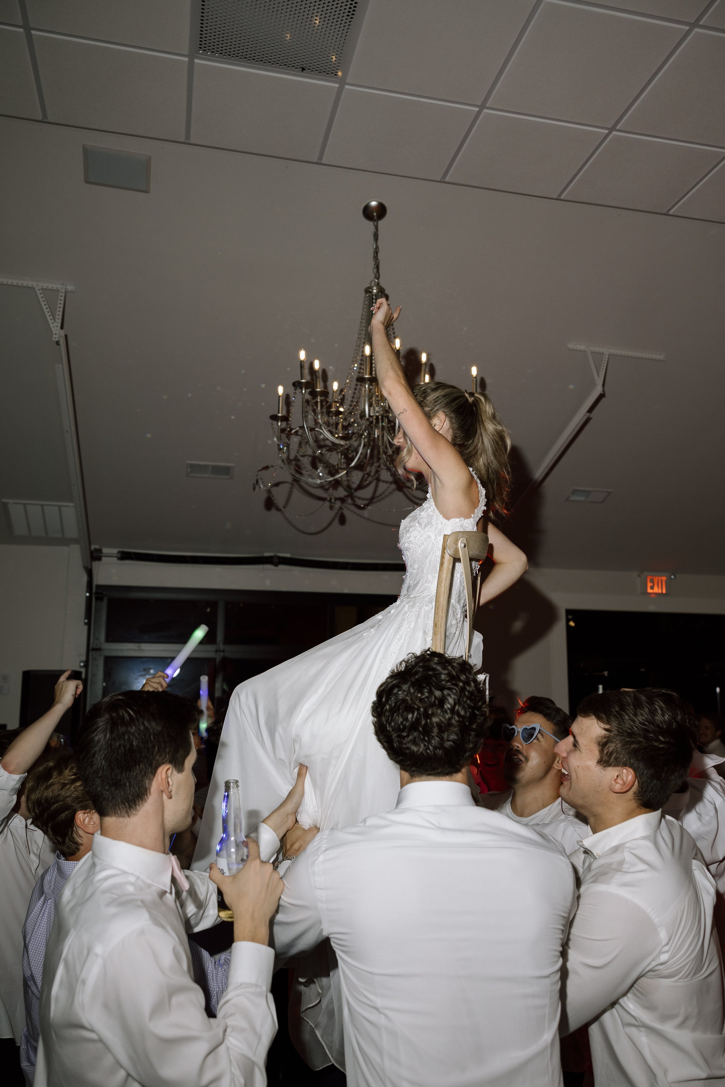 A bride in a wedding dress being lifted on a chair by a group of men during a wedding celebration