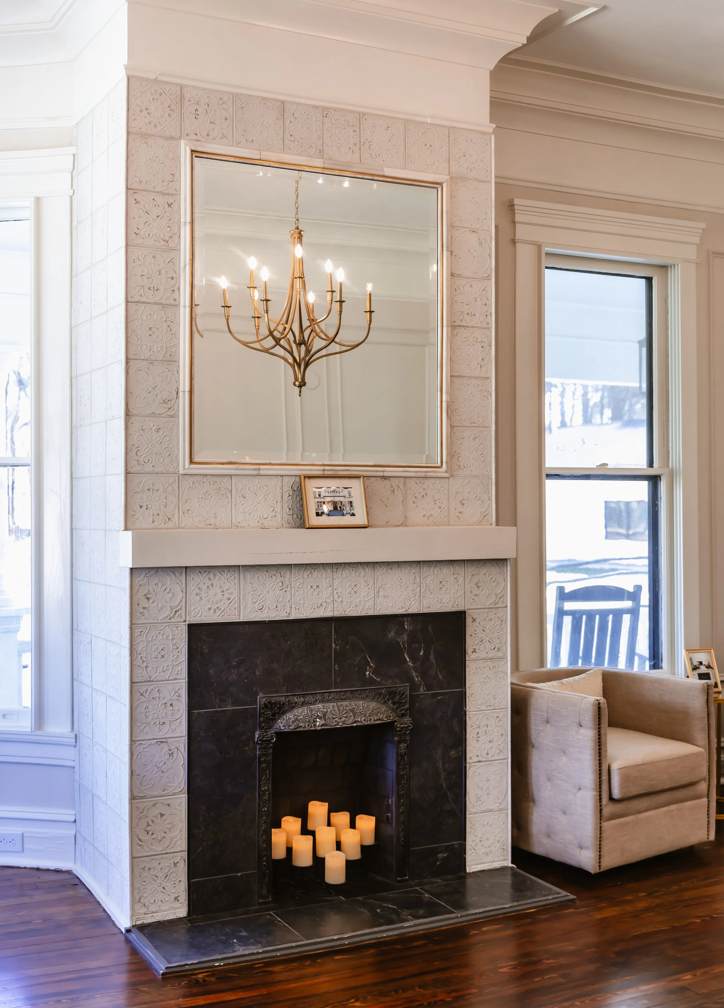 Living room with fireplace, large mirror, chandelier, and window showing snowy outdoor scene.