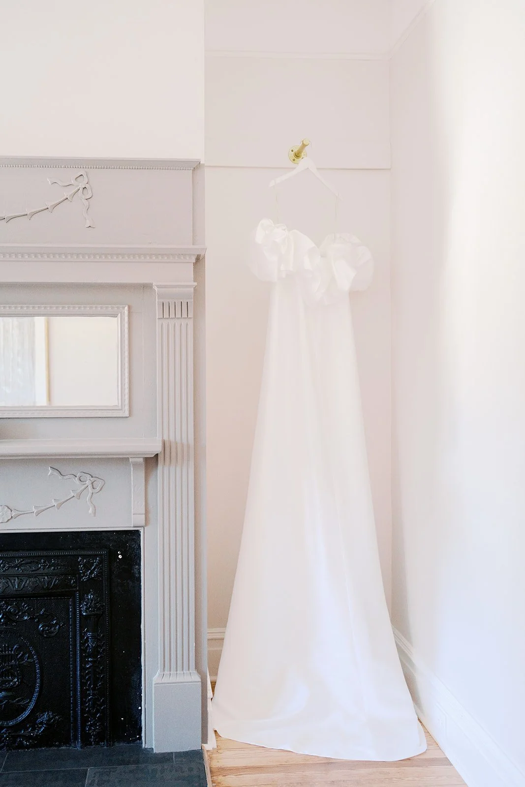 A white wedding dress hanging on a hook on the wall next to a fireplace mantel.