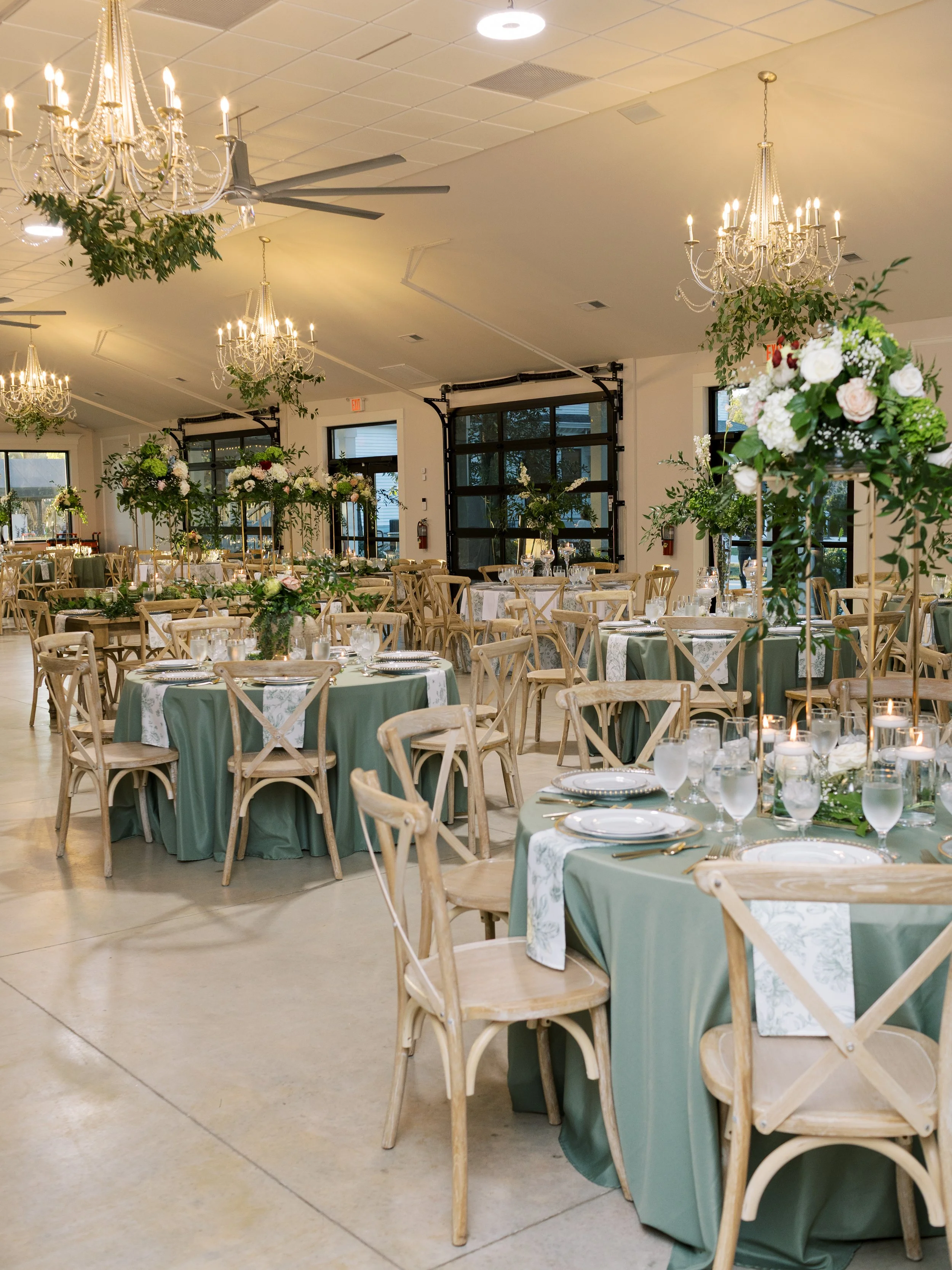 Elegant event space decorated with chandeliers, floral centerpieces, and tables with green tablecloths and white napkins.