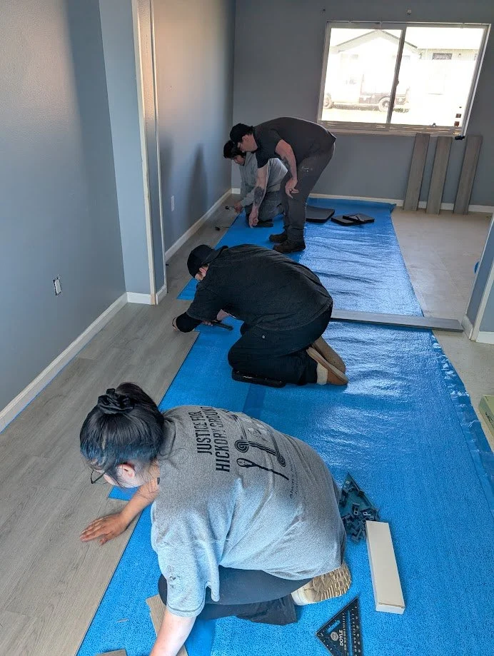 Three people installing flooring in a room, kneeling on blue protection mats.