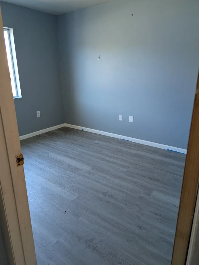 Empty room with light gray walls, a small window, and gray wood-style flooring, possibly newly renovated.