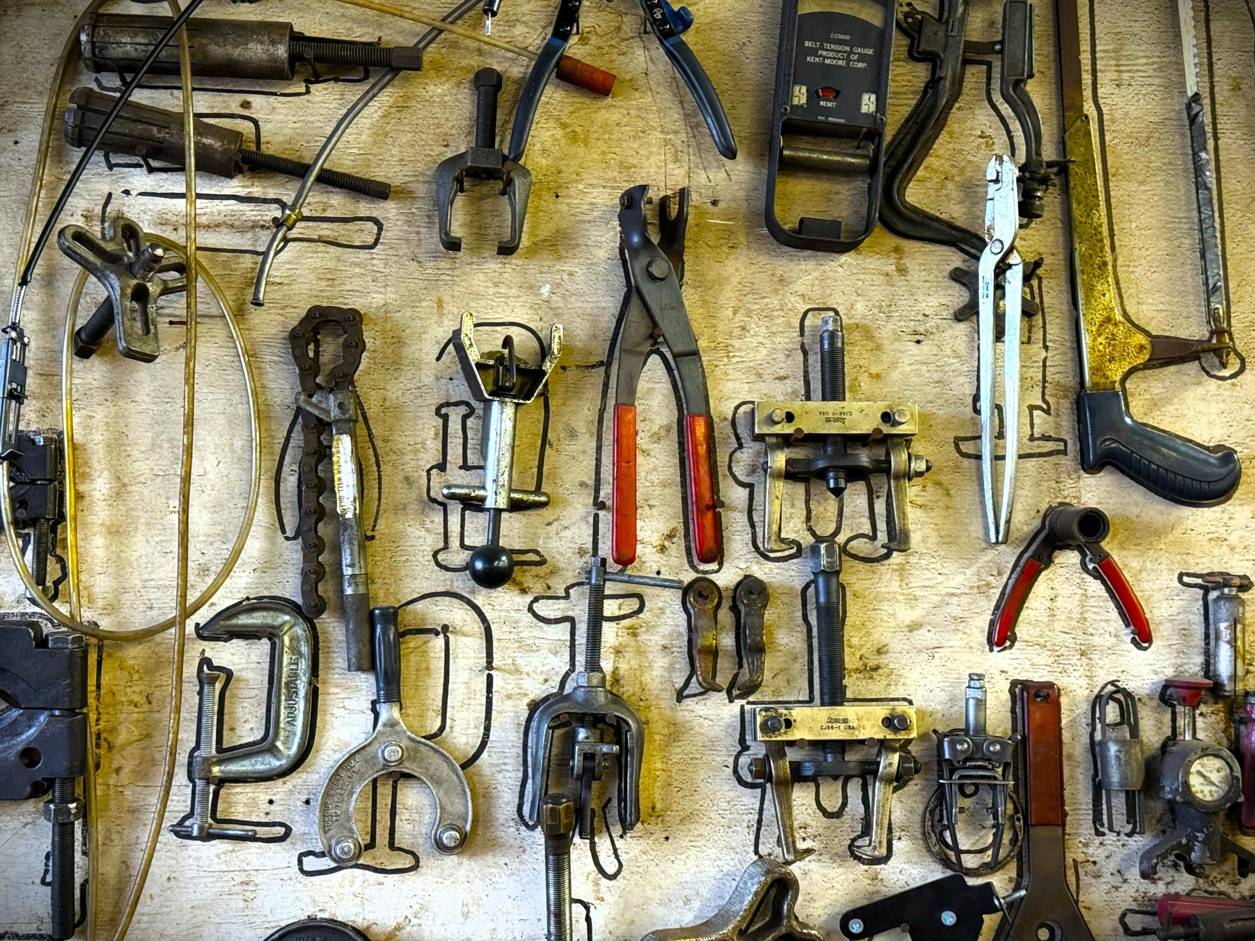 Various hand tools and mechanical parts laid out on a wooden surface, including pliers, wrenches, clamps, a chain, and other metal tools.