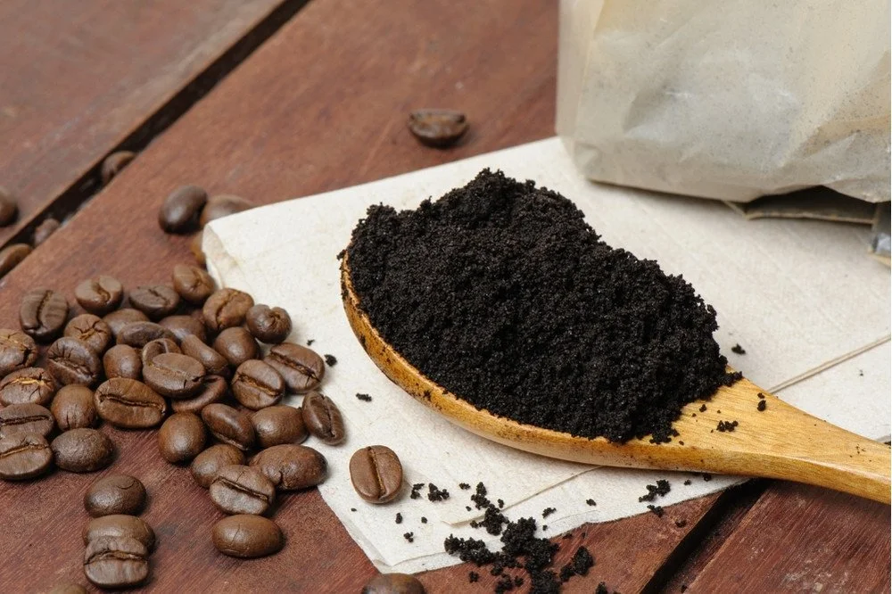 Coffee grounds on a wooden spoon resting on a wooden table with coffee beans