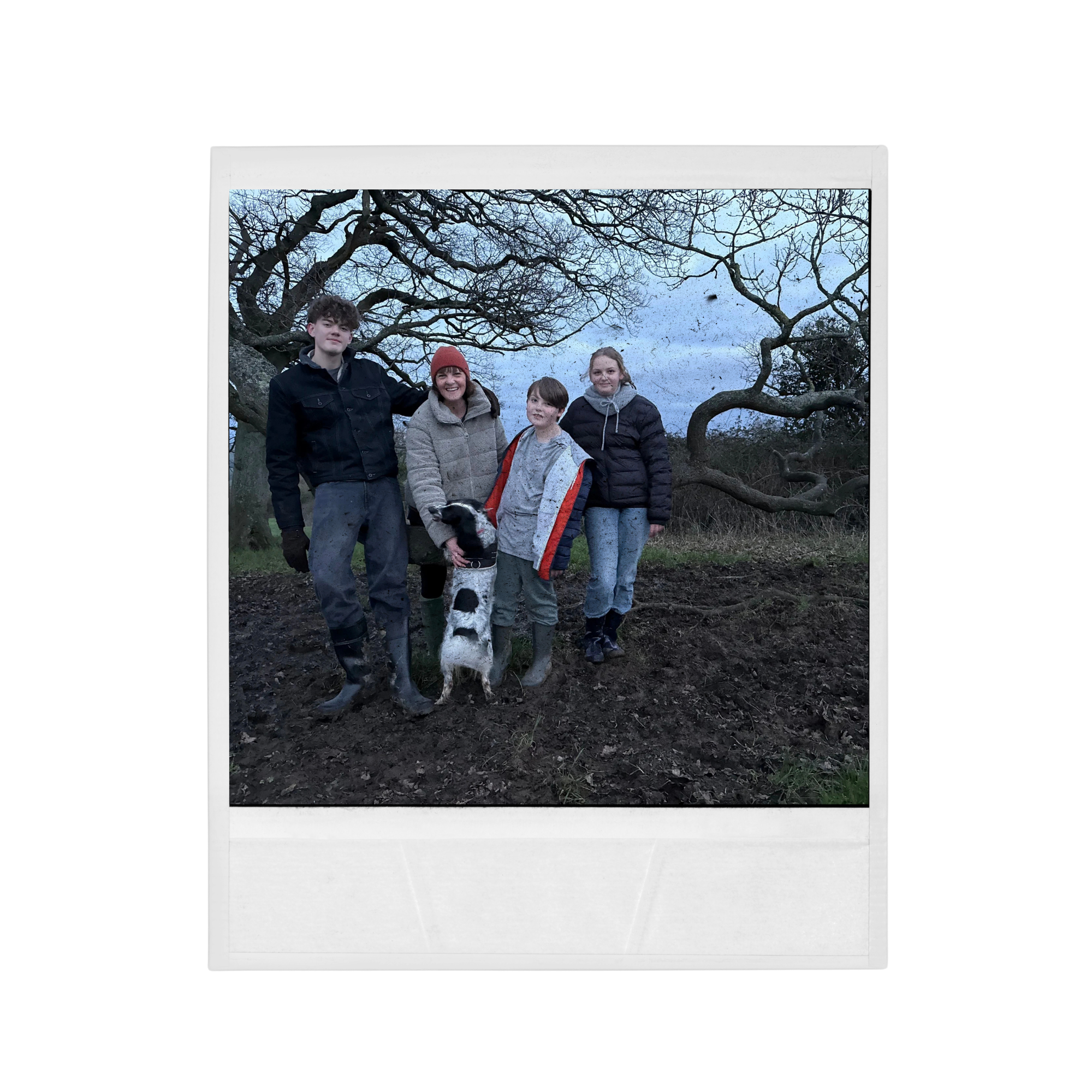 A group of four people and a dog standing outdoors in front of leafless trees. It appears to be late fall or winter, and the sky is cloudy.
