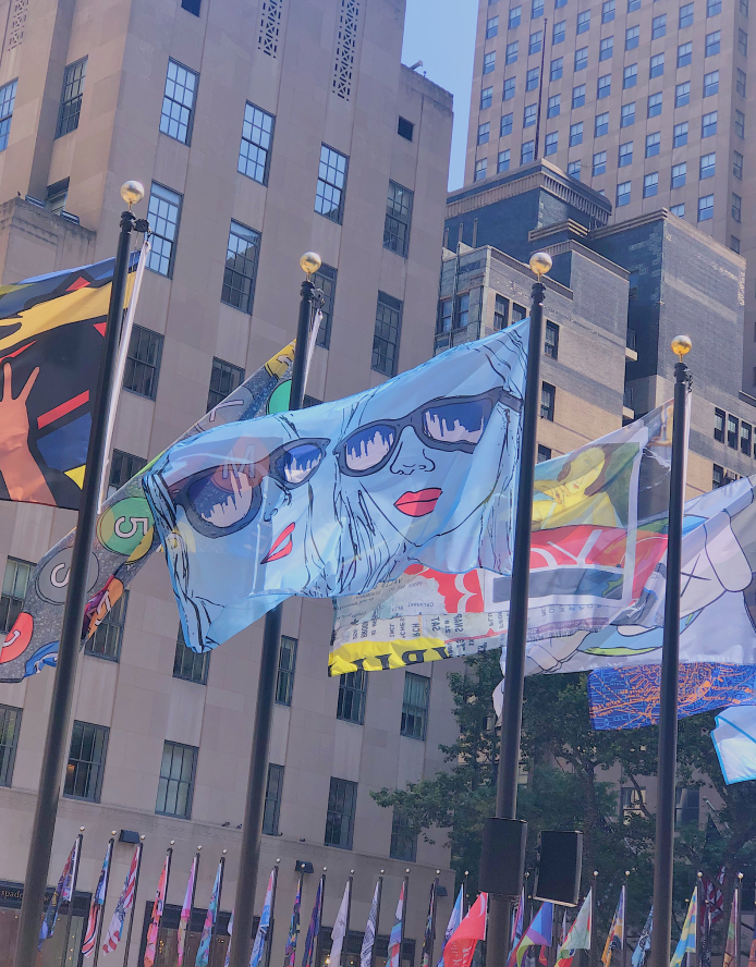 Flags flying on flagpoles in an urban area with tall buildings in the background.