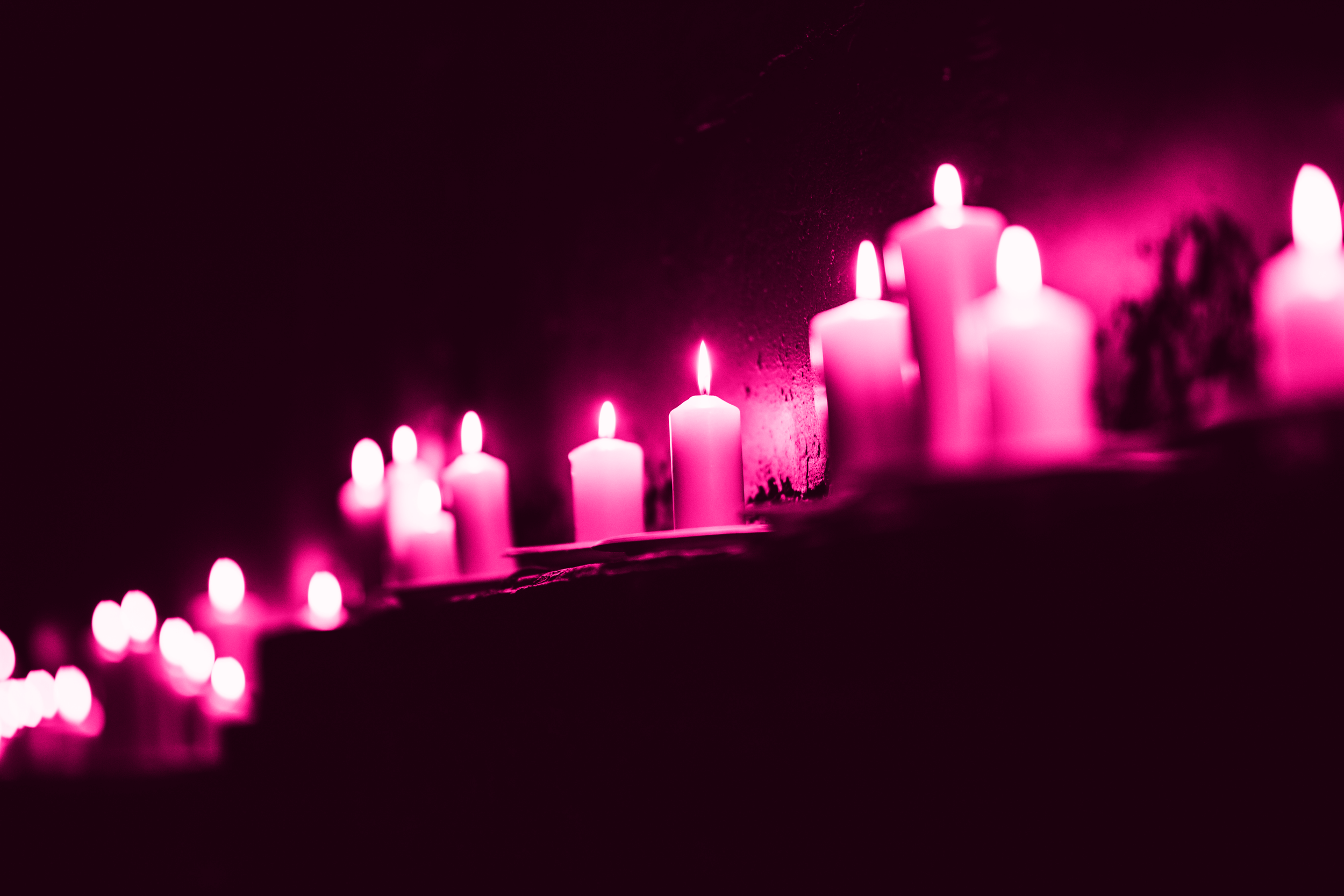Multiple pink candles are burning against a dark background, creating a soft glow.