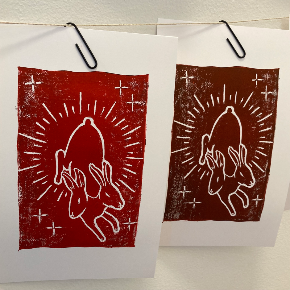 Two prints of a stylized graphic of a two-headed rabbit in white on a red background, hanging with paper clips on a string.