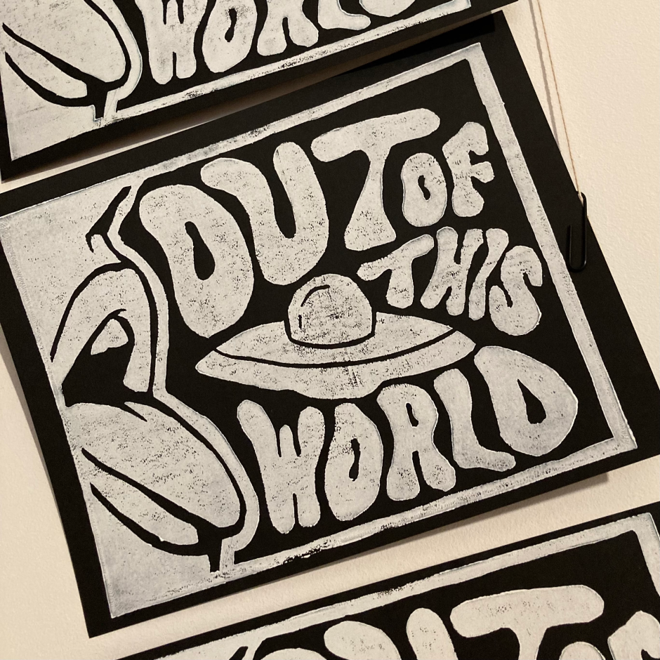 Black and white print with stylized text reading 'Out of this world,' featuring a drawing of a UFO flying into a mouth.