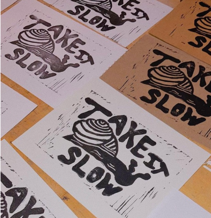 Multiple printed posters with the message "Take It Slow" and an illustration of a snail, arranged on a wooden surface.