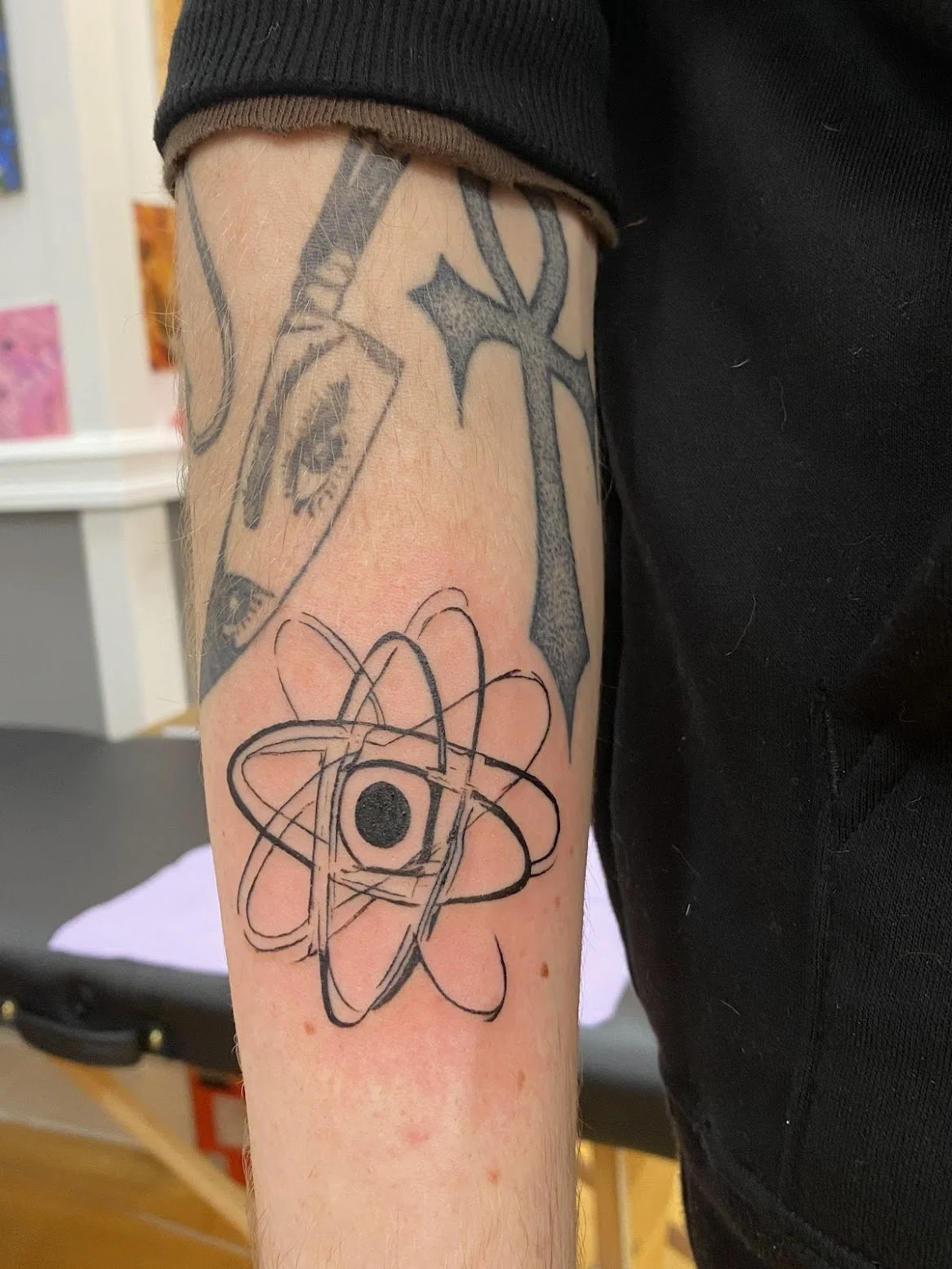Tattoo of an atomic model on a person's forearm with a black circle in the center and overlapping elliptical orbits.