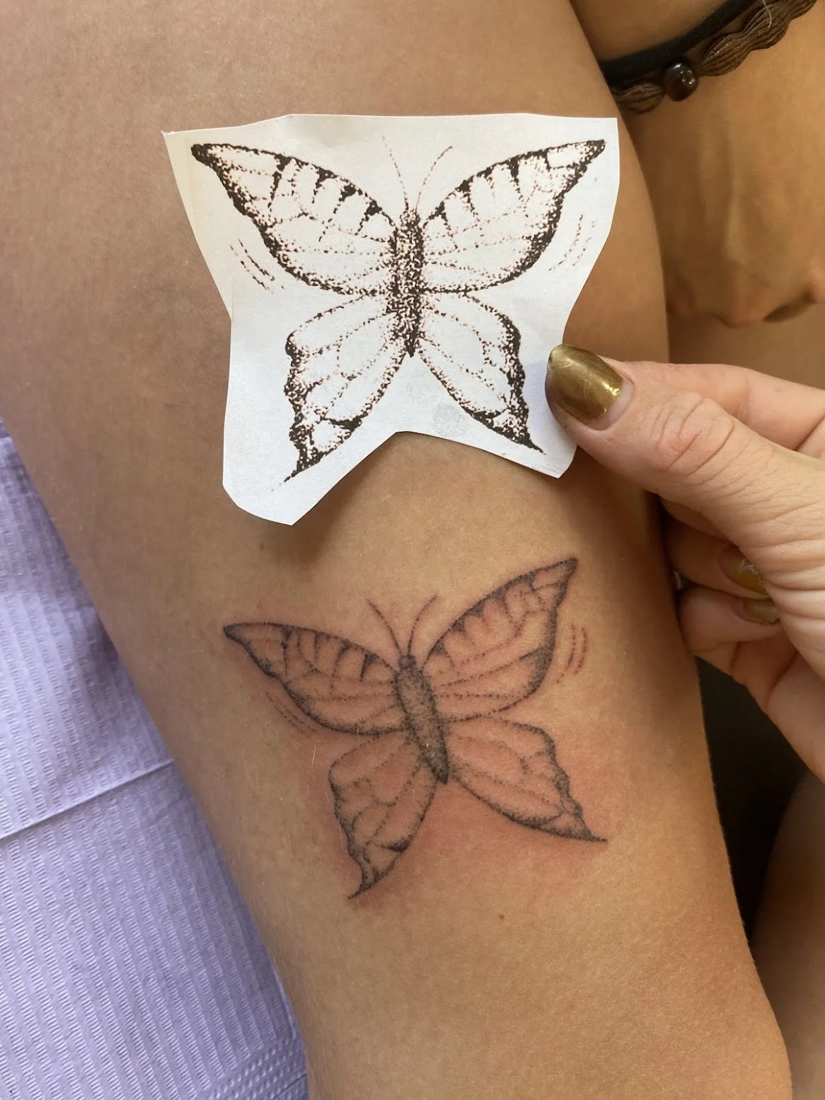 A tattoo of a butterfly on someone's arm, with a tattoo stencil being applied over it.