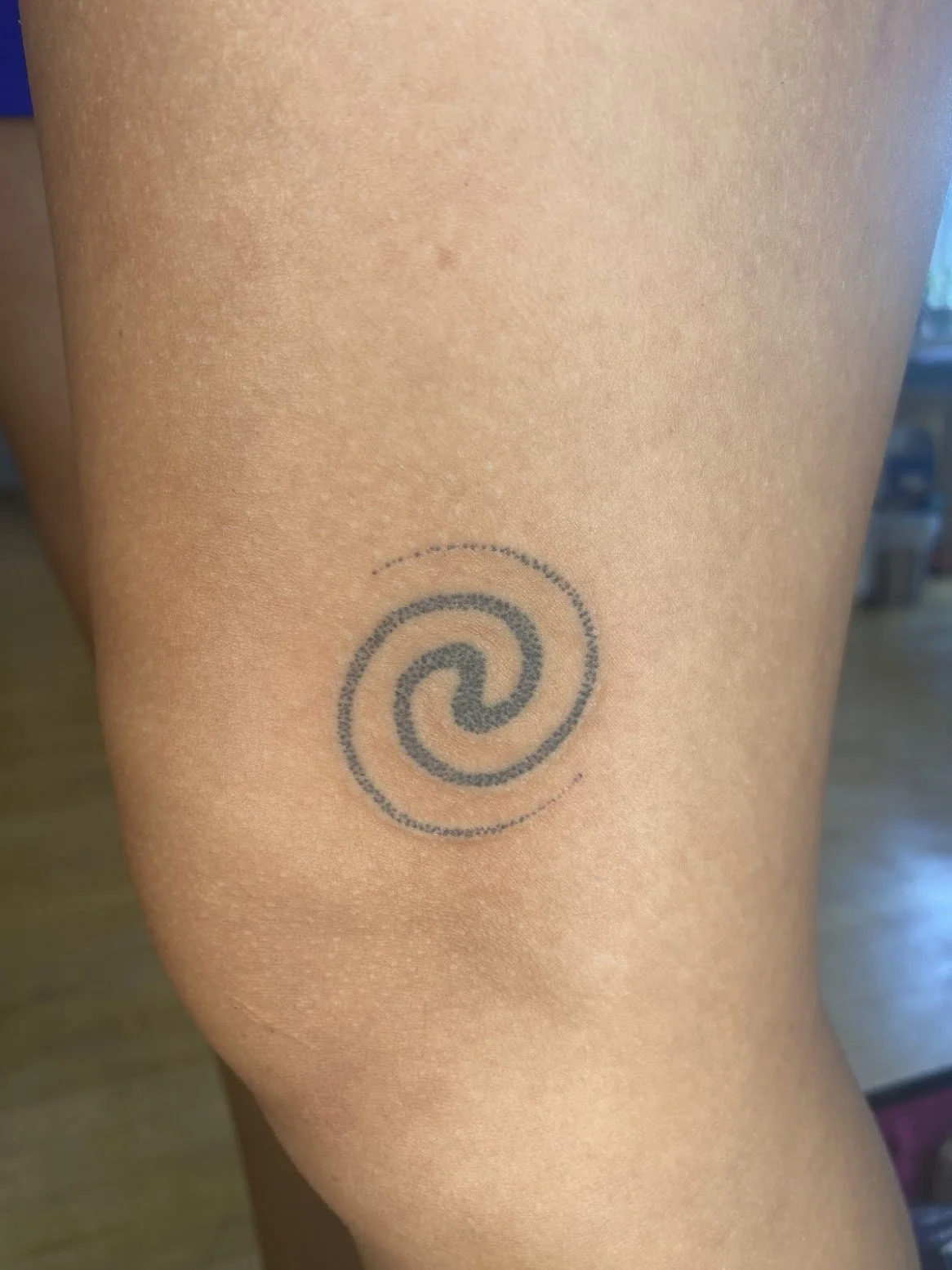 Close-up of a person's thigh with a small spiral tattoo on the skin.