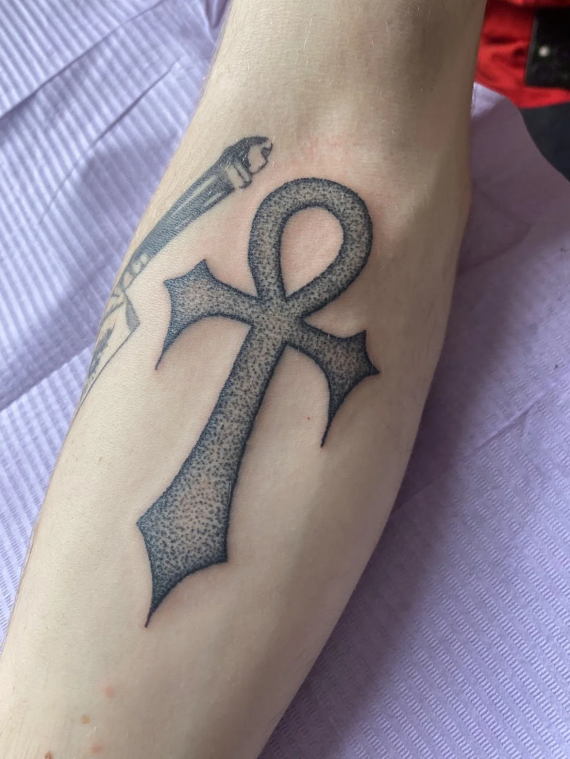 Tattoo of an ankh with a stippled, textured, dotted shading pattern on a person's arm.