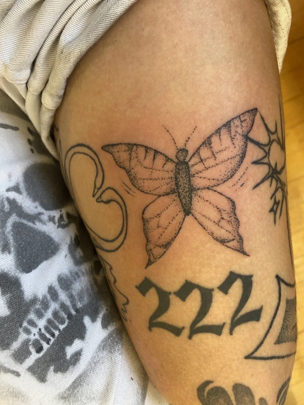 Tattoo of a butterfly on a person's thigh, with the number 222 below it.