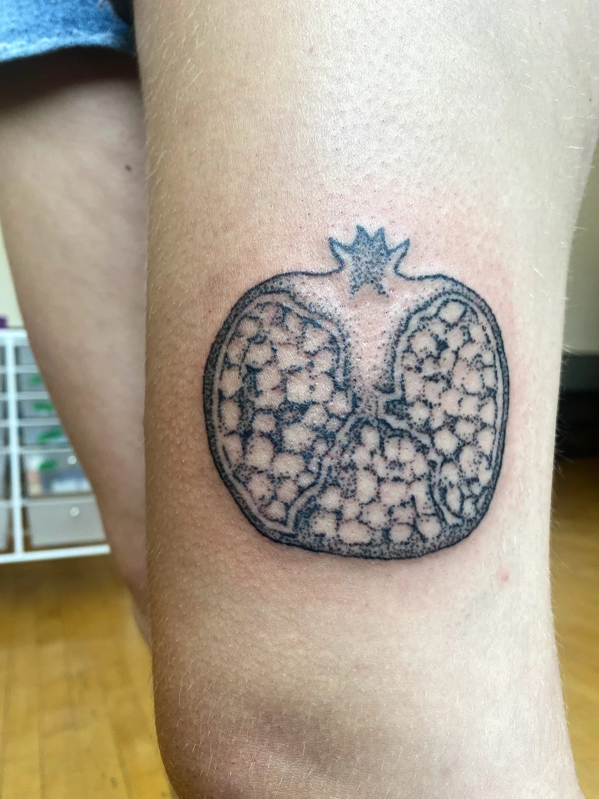 Tattoo of a pomegranate, featuring a detailed interior pattern, on a person's leg.