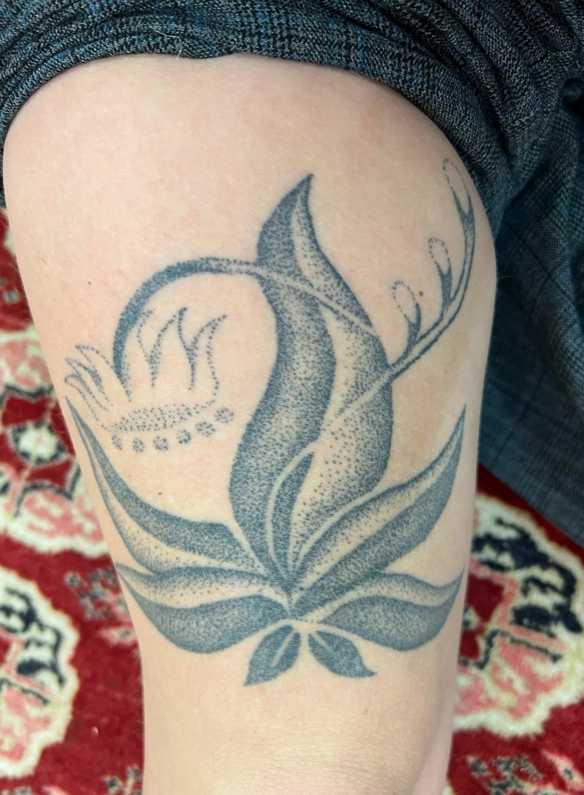A tattoo of a stylized flower with leaves, Four Agreements cover design, on a person's thigh.