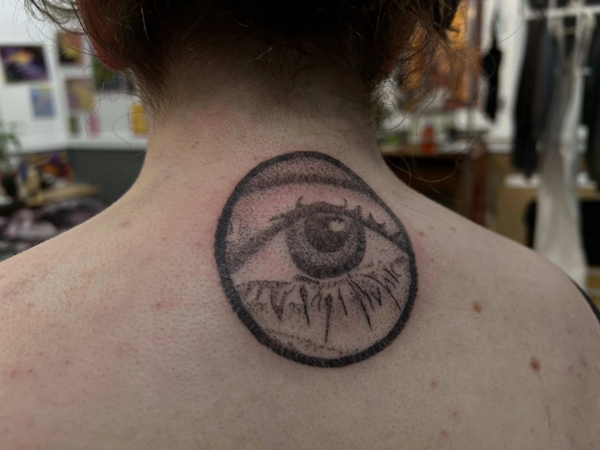 Tattoo of a detailed eye inside a circle on woman's upper back.