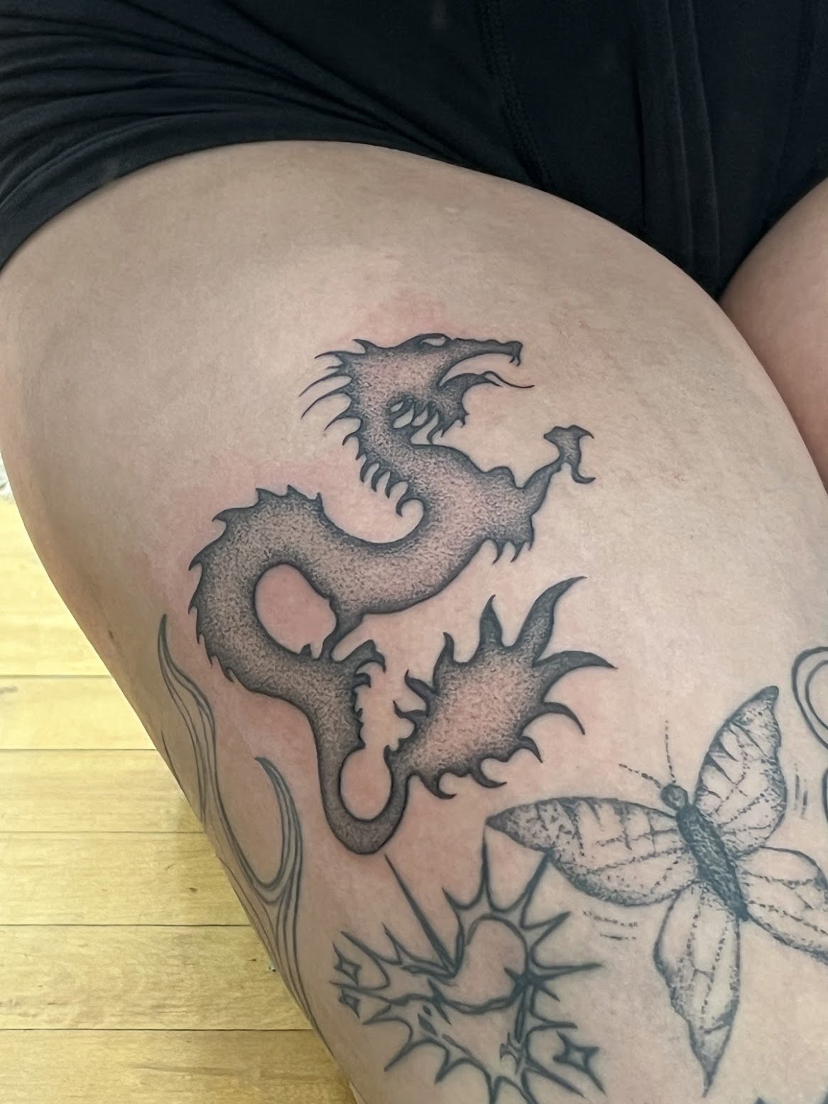 Tattoo of a dragon and a butterfly on a person's thigh.