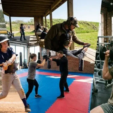 Two kids practicing boxing with an instructor at an indoor training facility, while others train outdoors on a bench