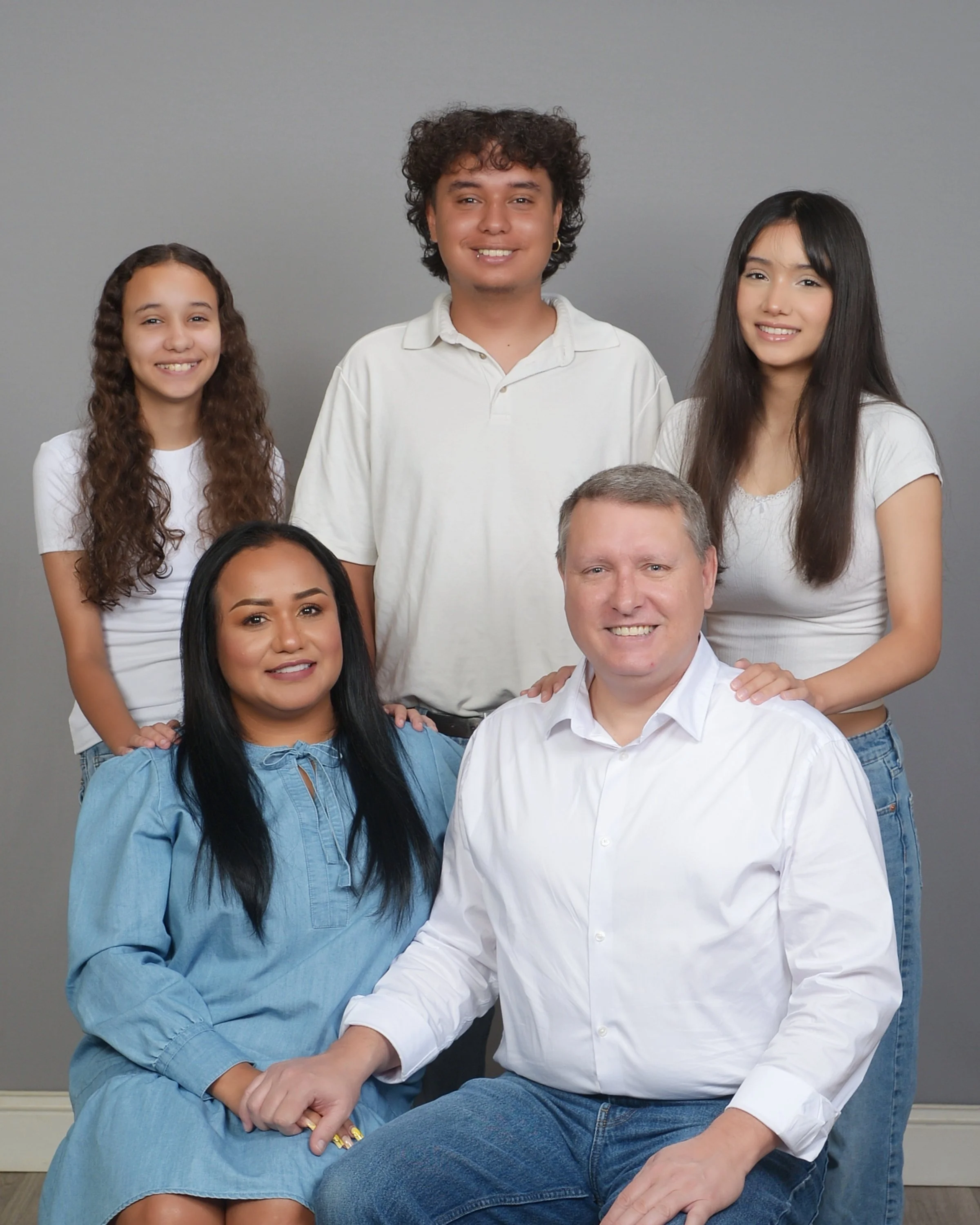 A family of six posing together against a plain gray background, smiling at the camera.