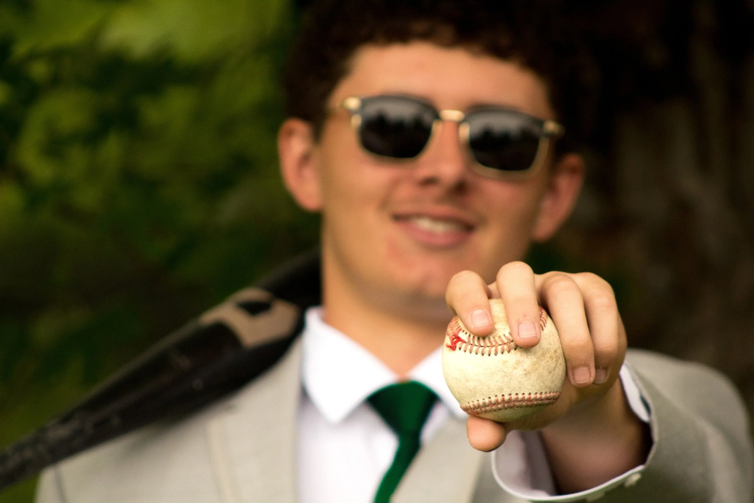 A person wearing sunglasses is holding and preparing to throw a baseball.
