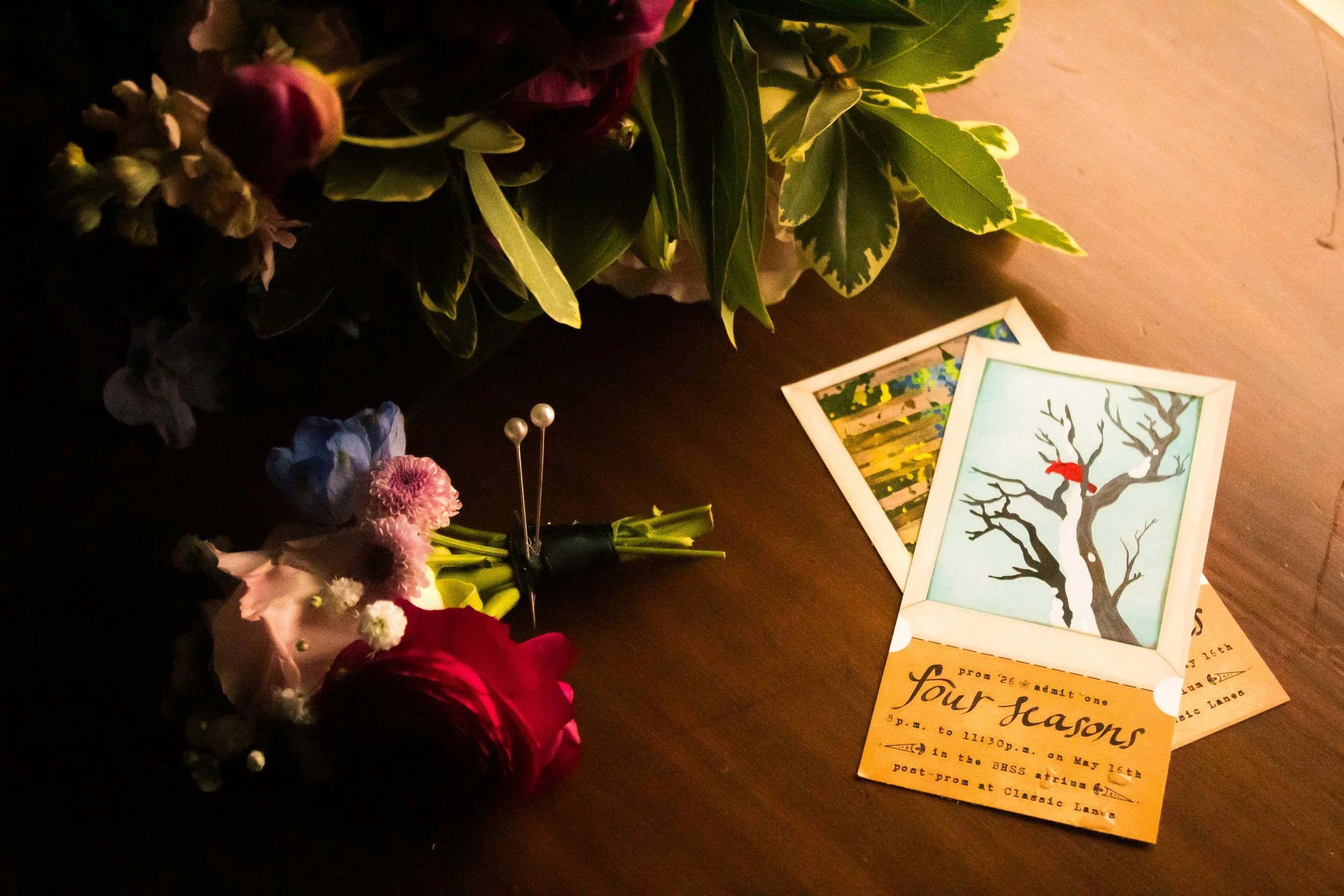 Flowers on a dark wooden surface with event flyers and small photographs of landscape art.