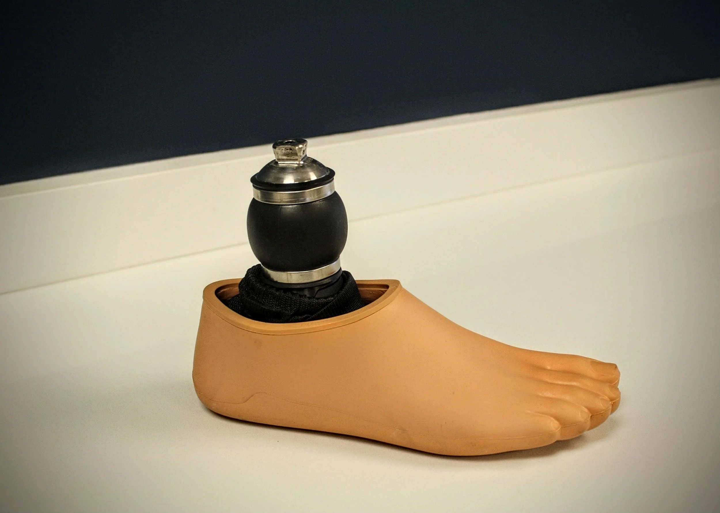 An Ossur vertical shock prosthetic foot with a black attachment at the ankle and a beige plastic foot shape, placed on a white surface.