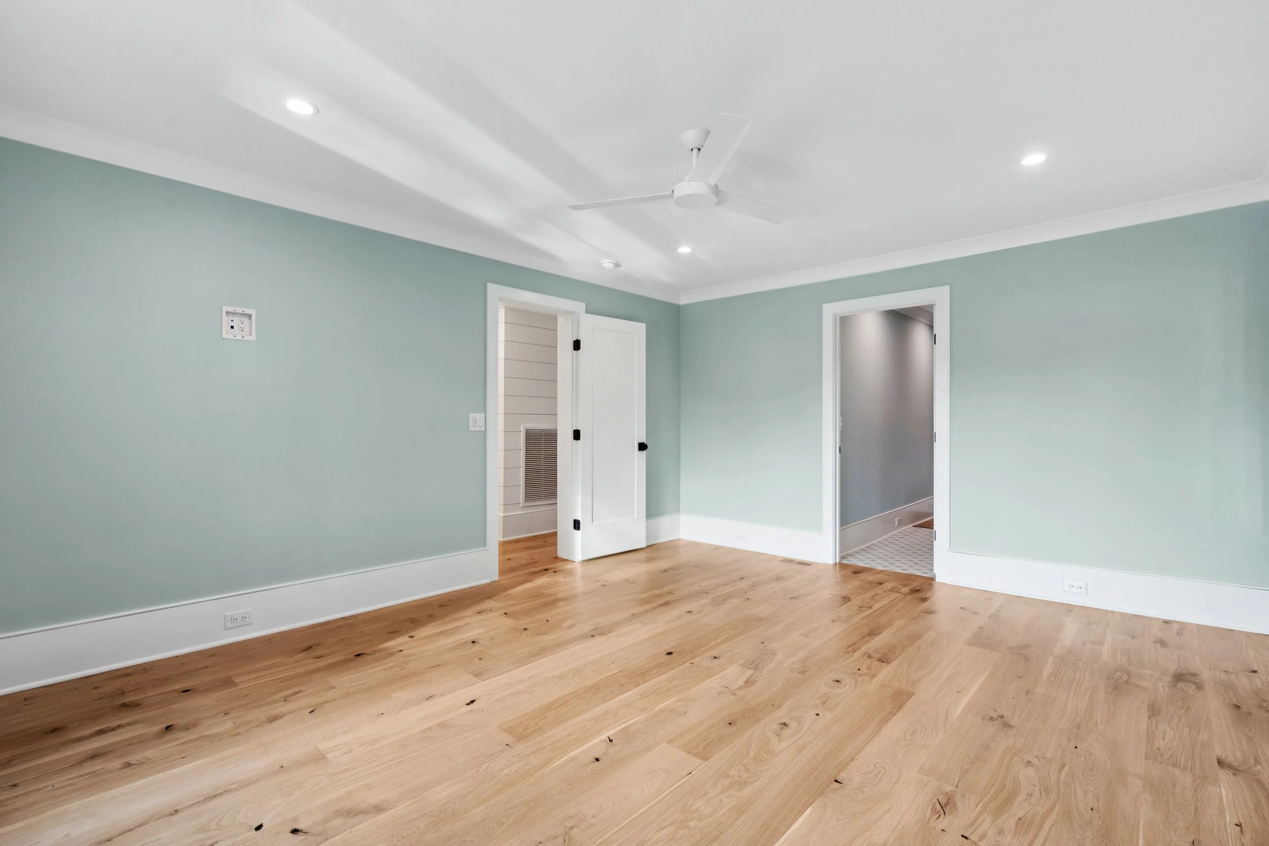 Empty room with light green walls, white trim, hardwood floors, ceiling fan, and two open doorways.