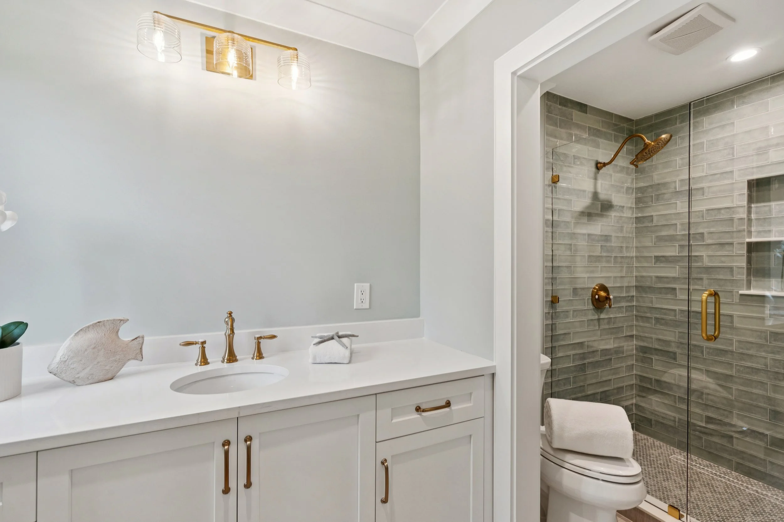 Bathroom with white vanity, gold fixtures, decorative fish, and a shower with glass door and gray tile walls.