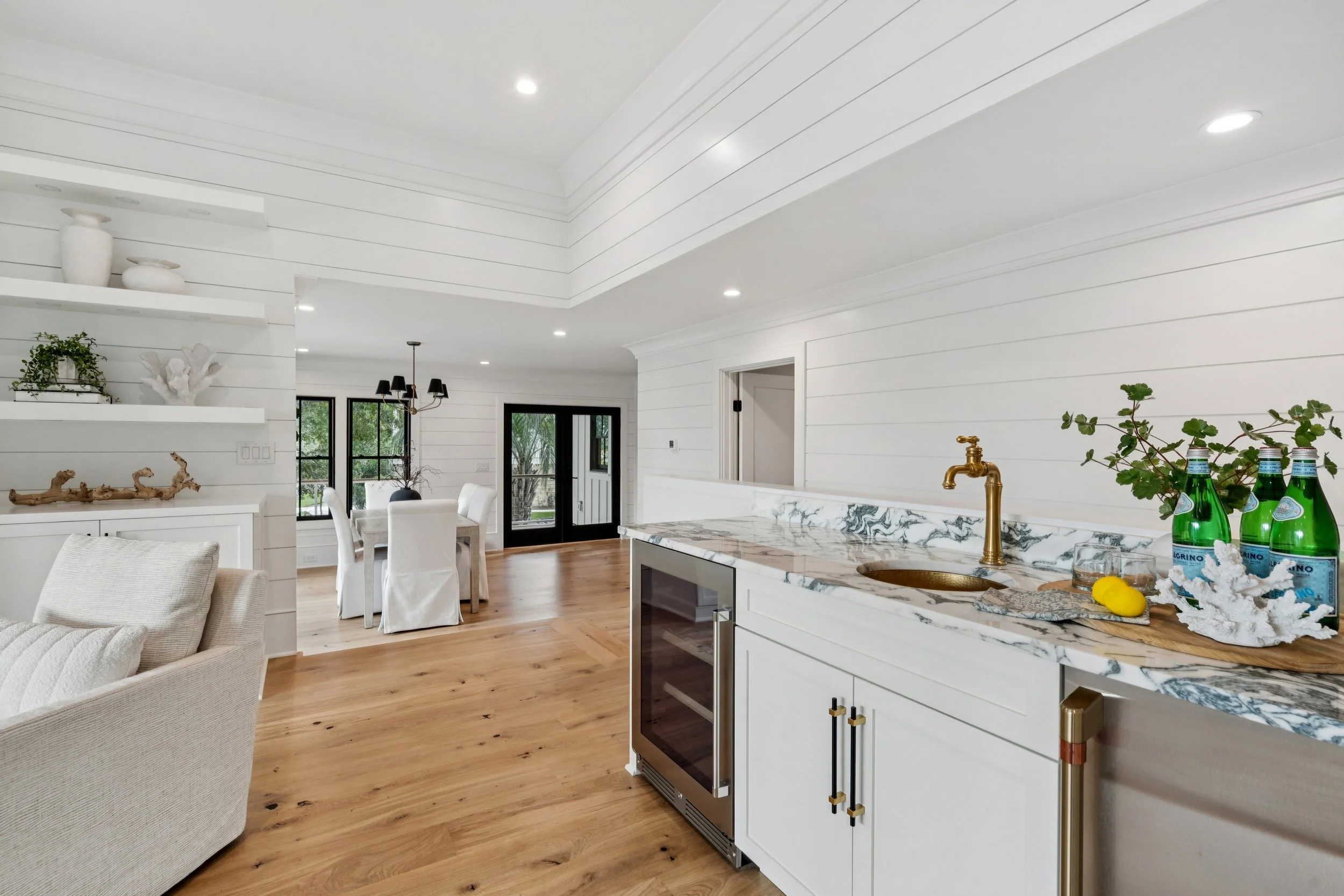 Open-concept living and dining area with white shiplap walls, hardwood floors, a kitchen with marble countertops, and sliding glass doors leading outside.