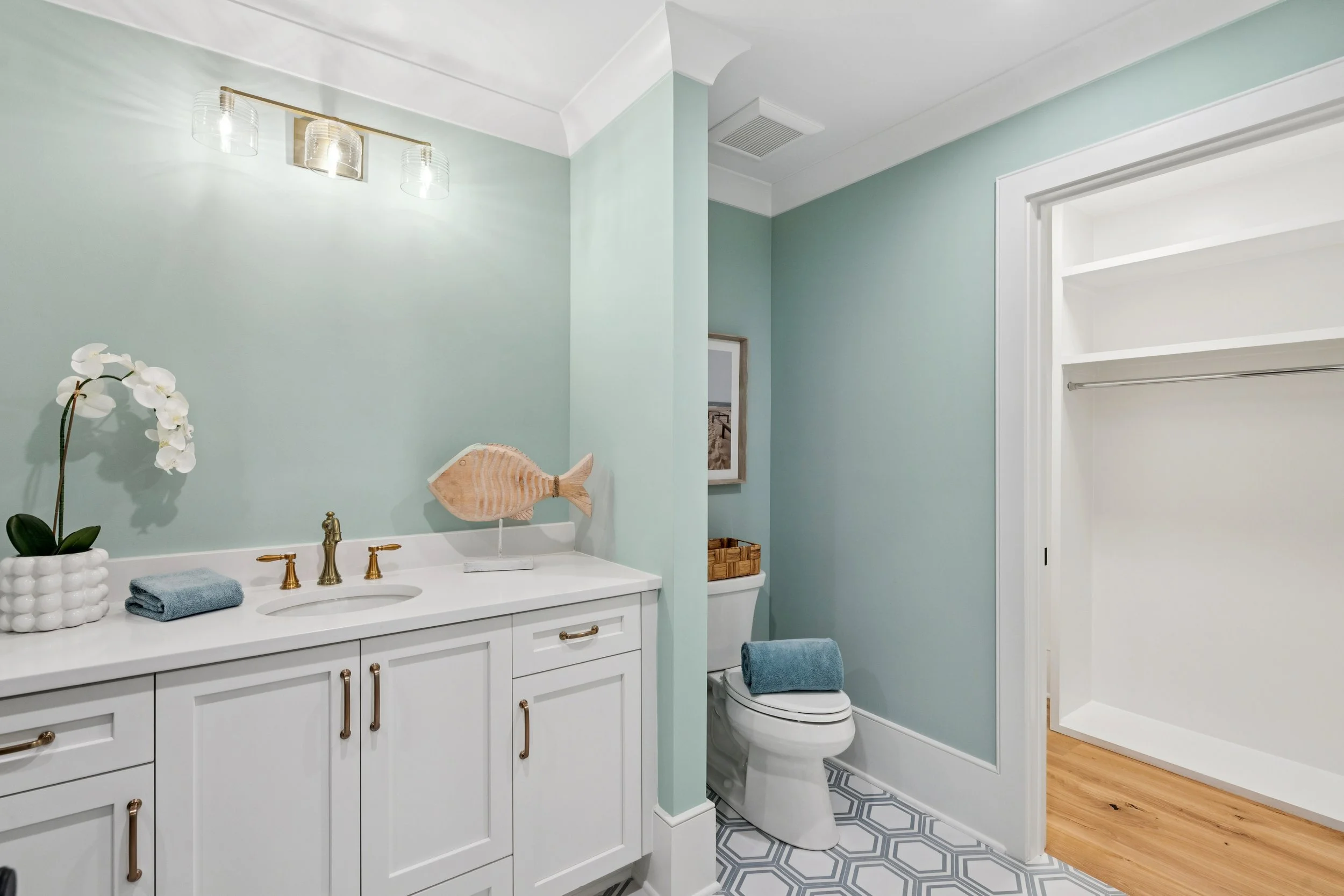 Bathroom with light teal walls, white cabinetry, gold fixtures, a fish sculpture, and decorative towels, with a separate closet space.