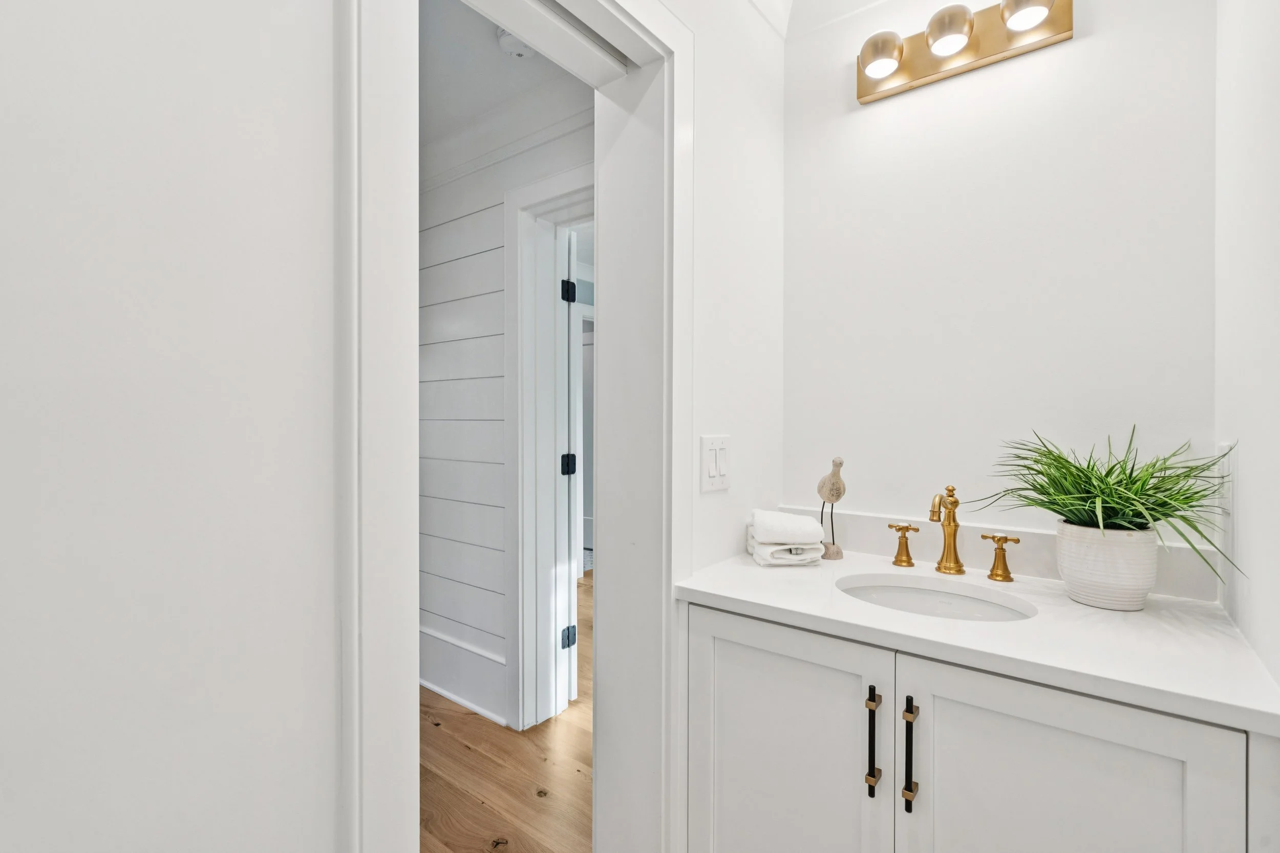 A bright white bathroom vanity with gold fixtures, a potted plant, and a small towel, with doors leading to other rooms