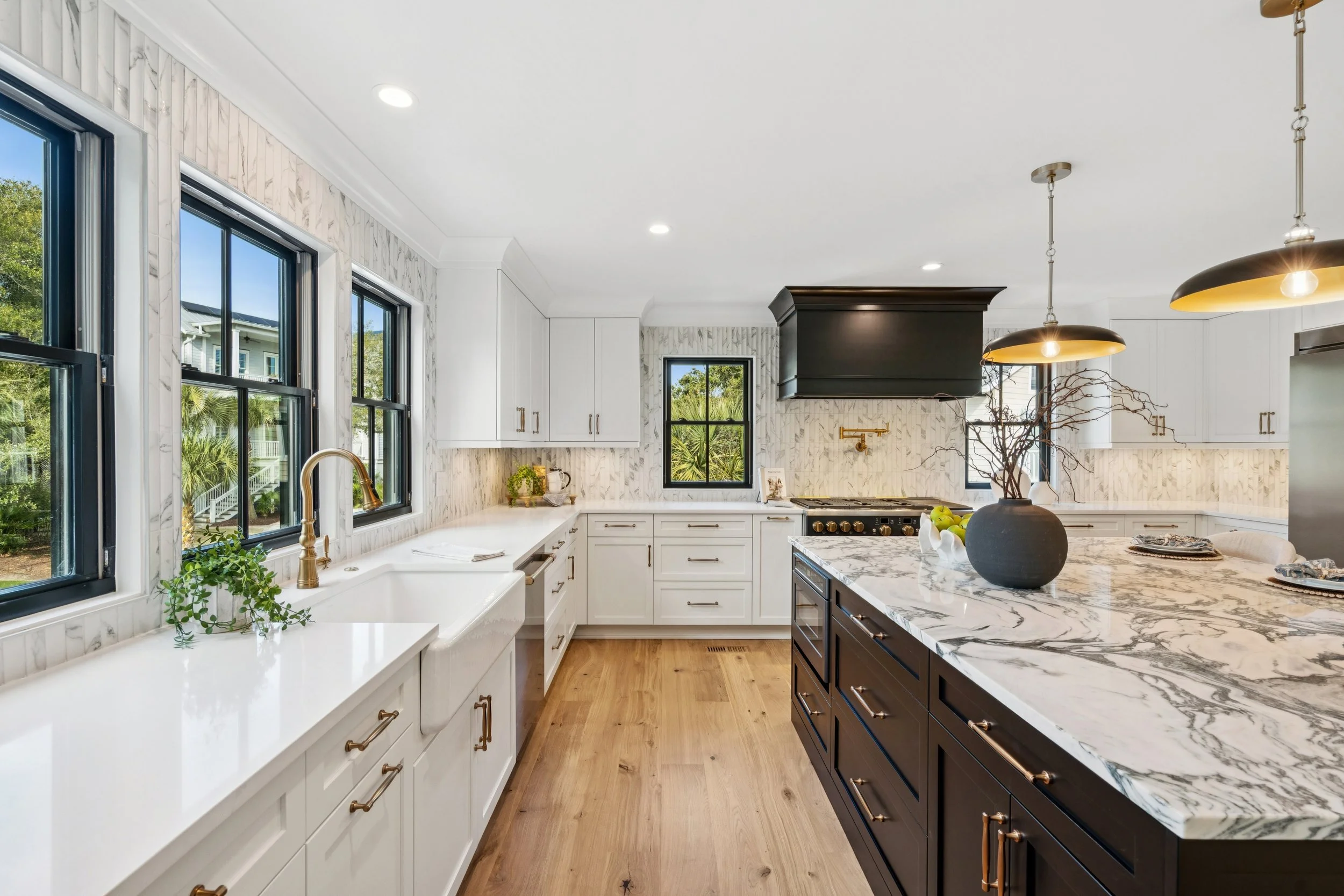 Modern kitchen with white cabinets, black island with marble countertop, hardwood flooring, and large windows