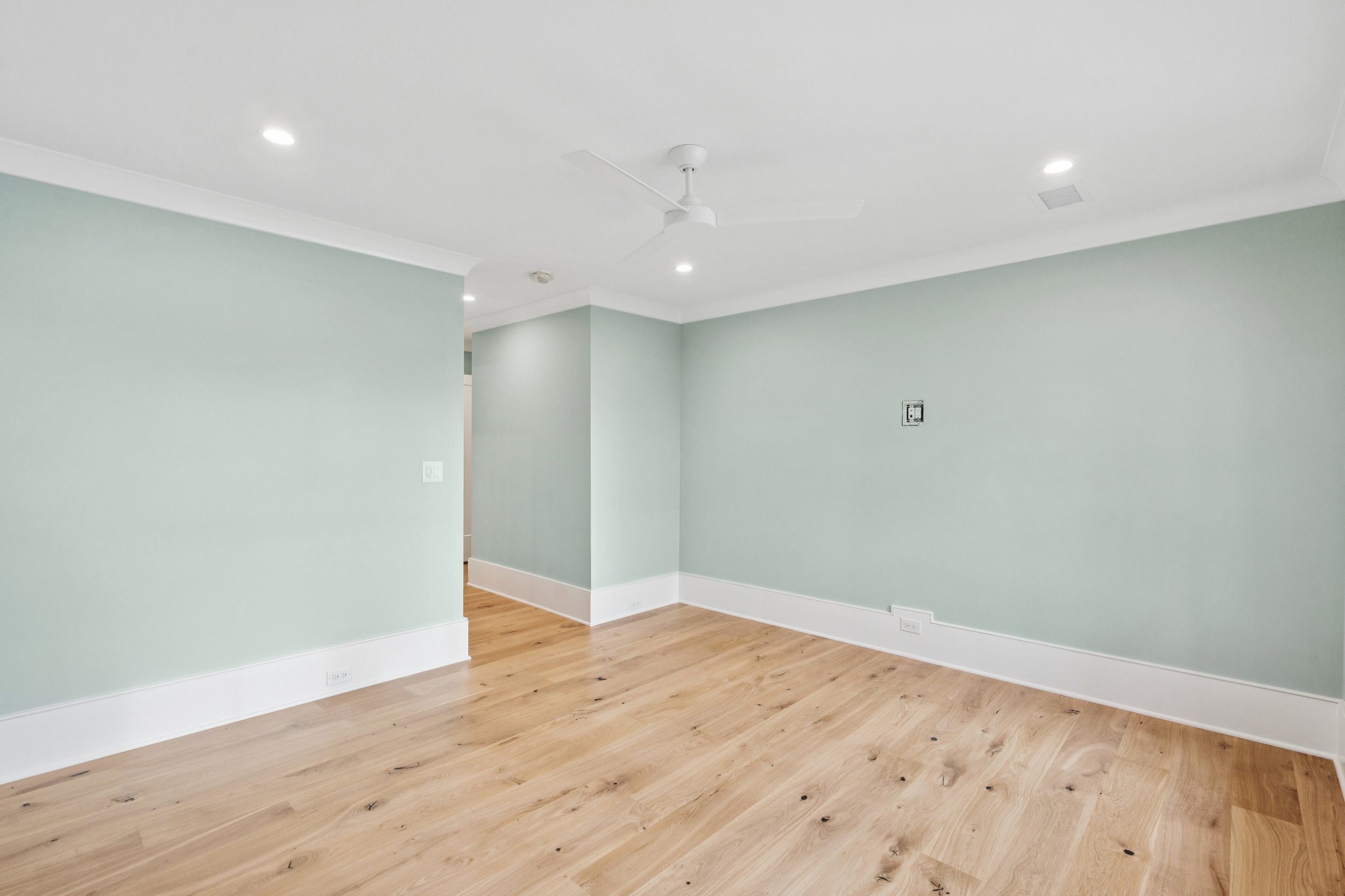 Empty room with light green walls, white baseboards, hardwood floors, ceiling fan, and recessed lighting.