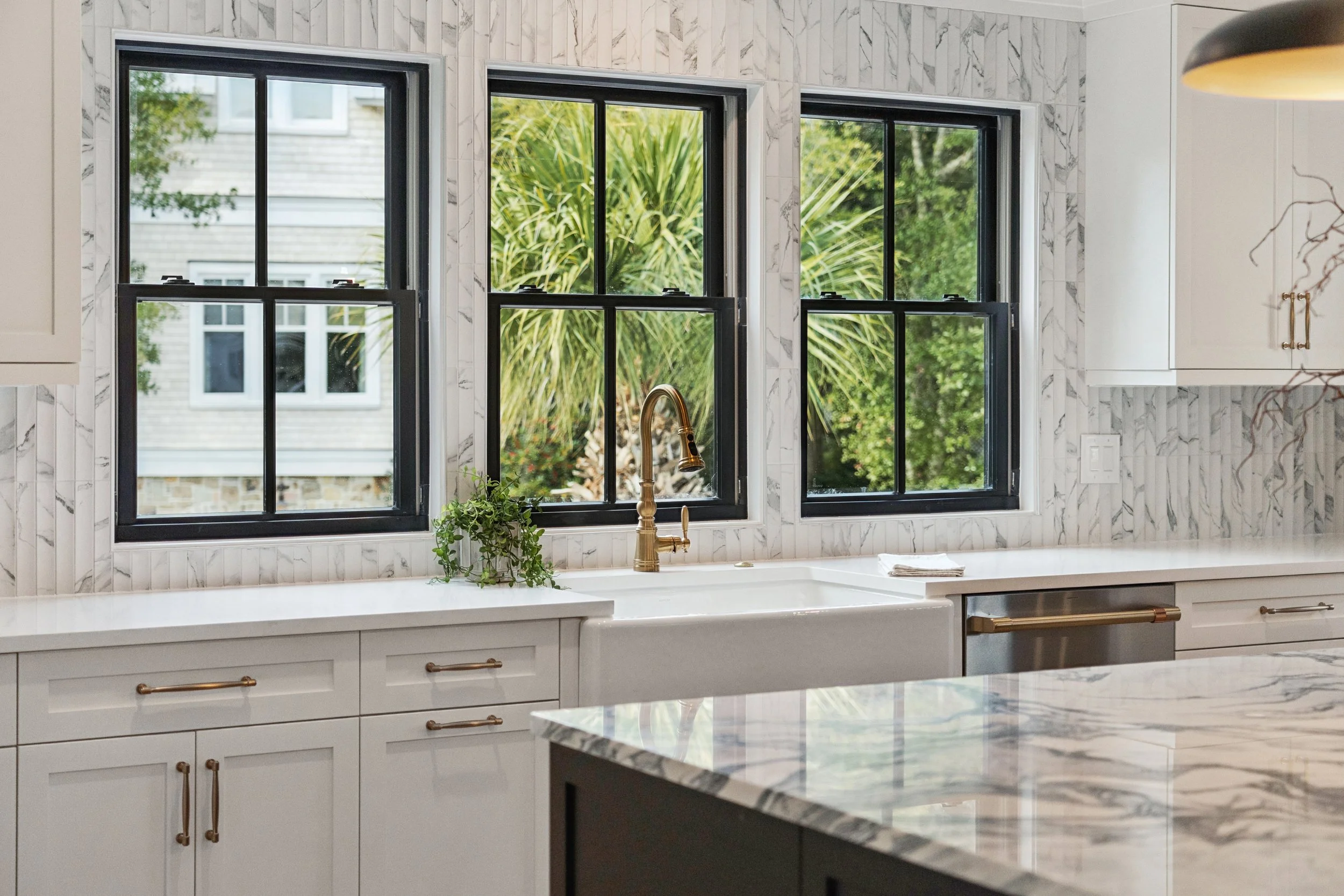 Modern kitchen with white cabinetry, a farmhouse sink, and black-framed windows showing greenery outside.